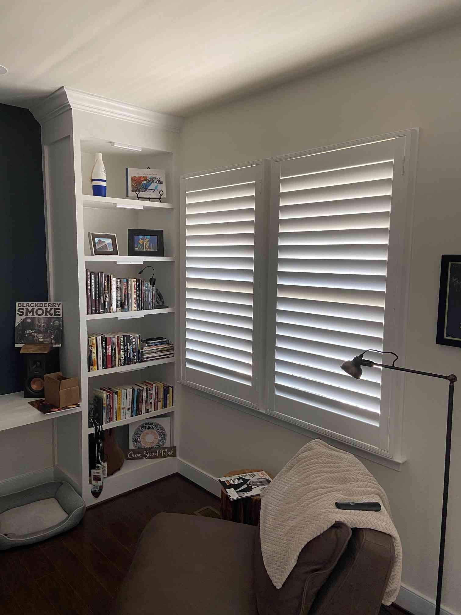 Cozy reading nook with bookshelves, shuttered windows, and an armchair in a bright corner room