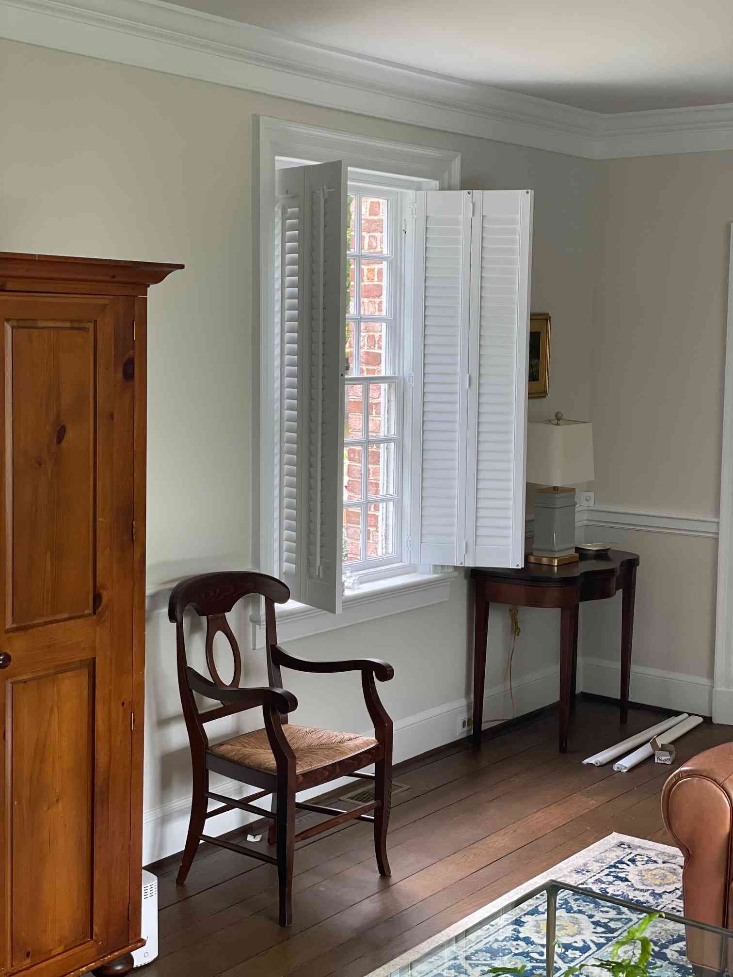 Sunlit room with white shutters, a wooden chair, wardrobe, and small desk on hardwood floor
