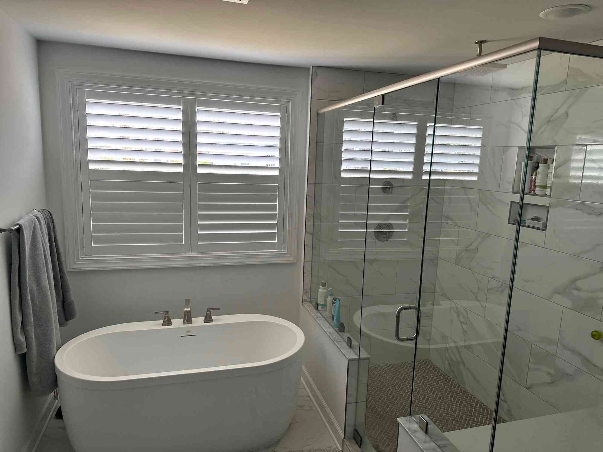 Bright modern bathroom with a freestanding tub, glass shower, and shuttered windows