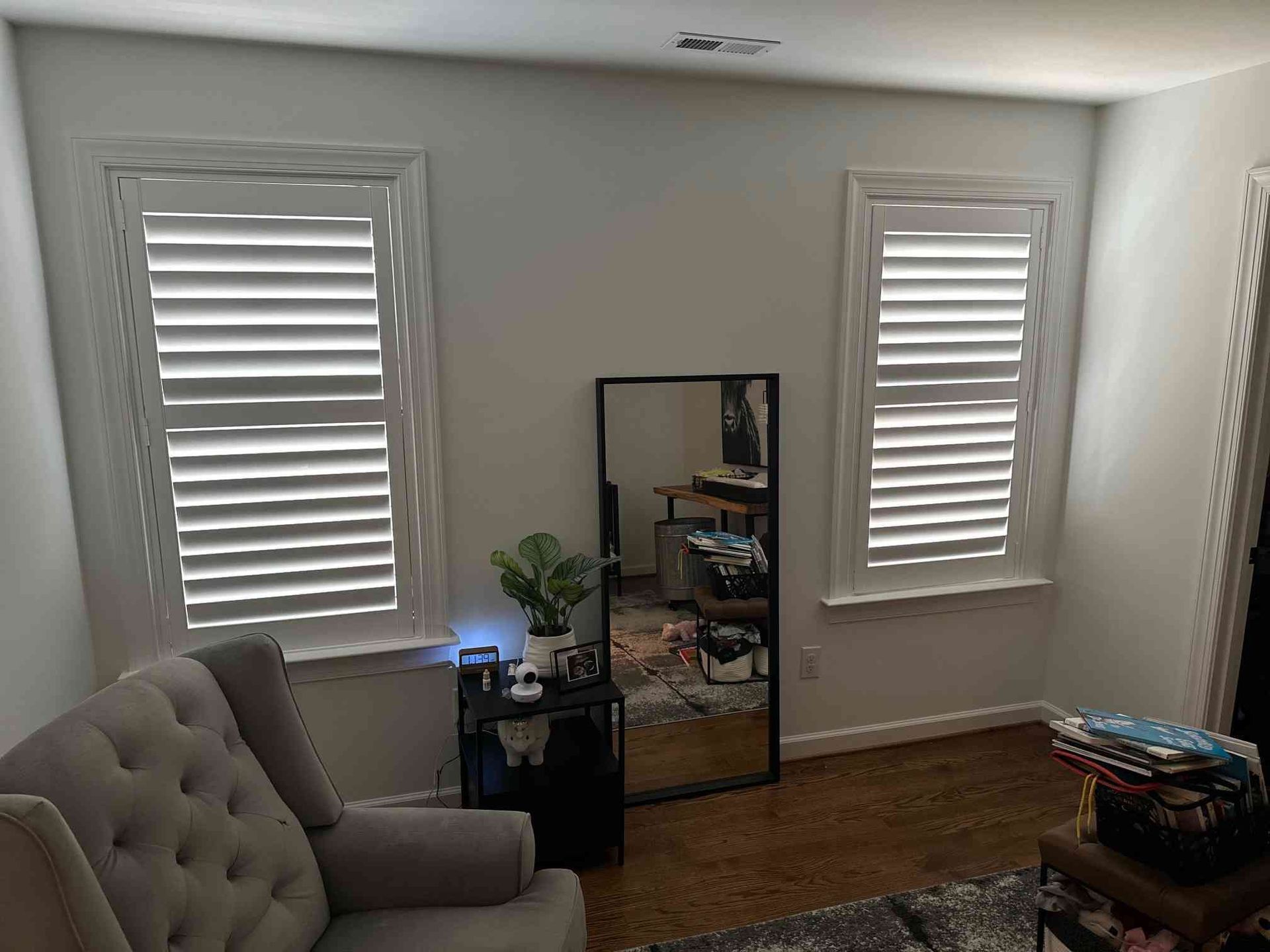 Bright room with two windows, a full-length mirror, armchair, side table, and hardwood floor.