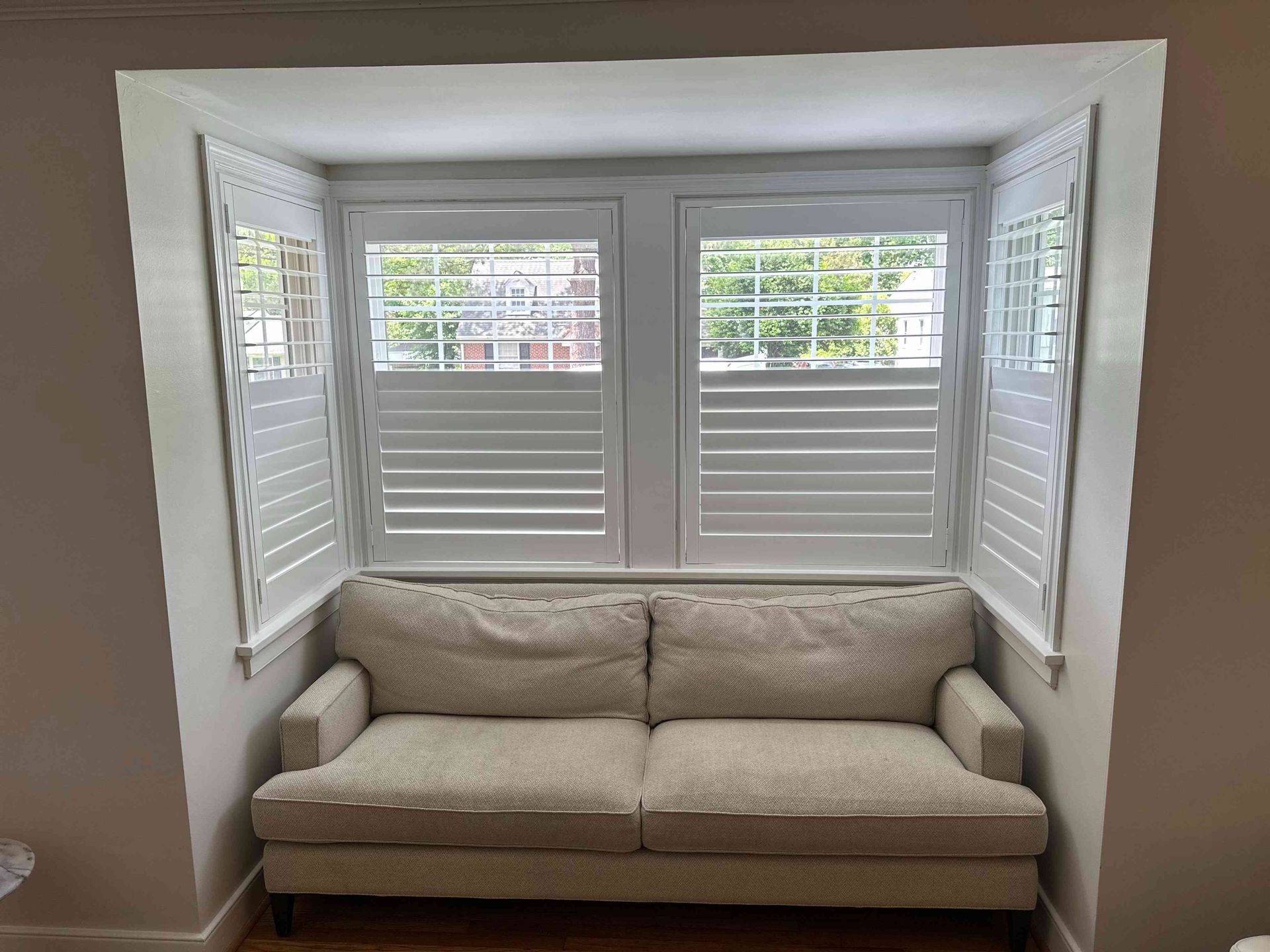 Built-in bay window seat with beige sofa and white shutters in a bright room