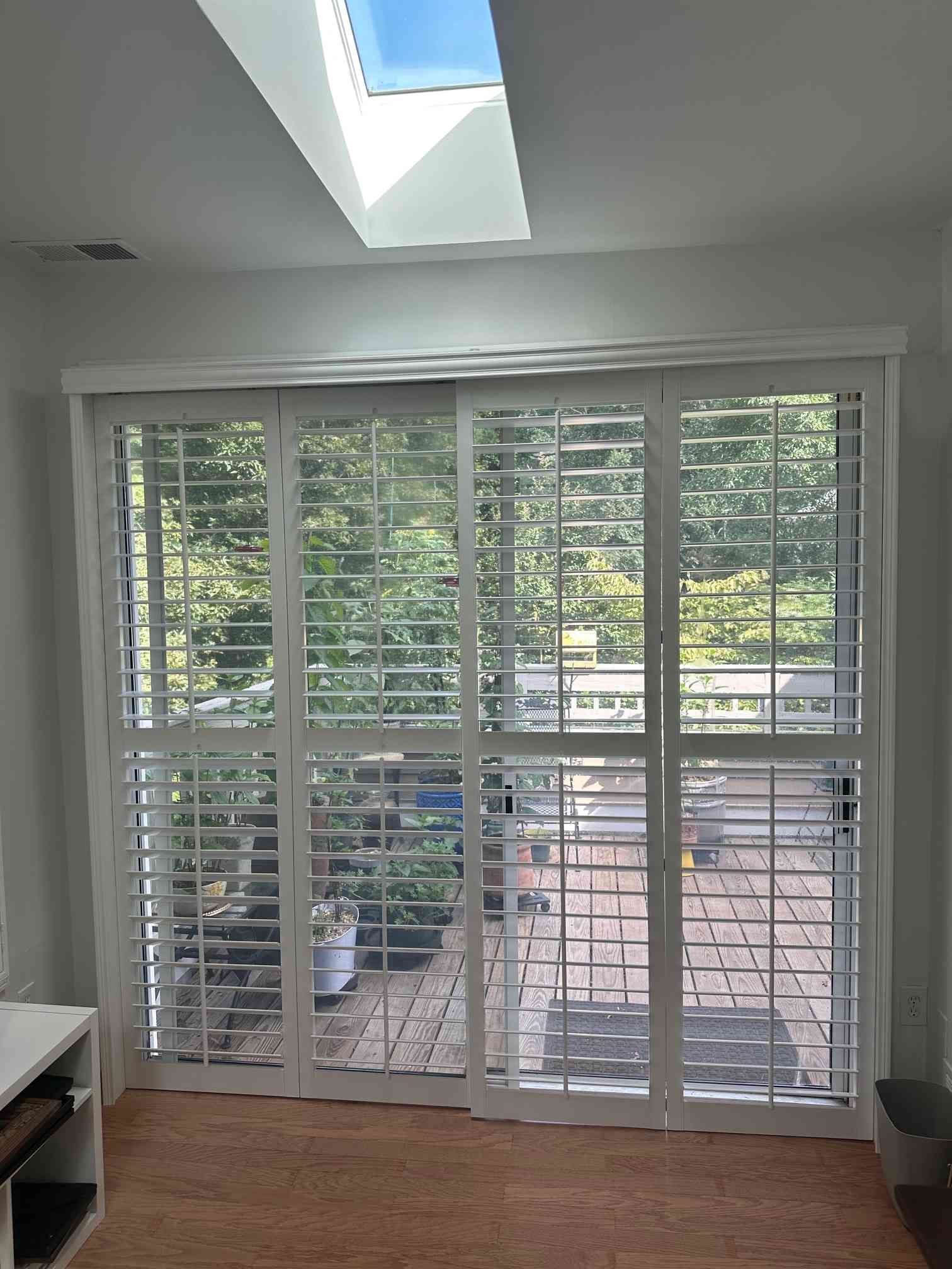Sunroom with skylight, white shutters, and sliding glass doors opening to a patio and trees