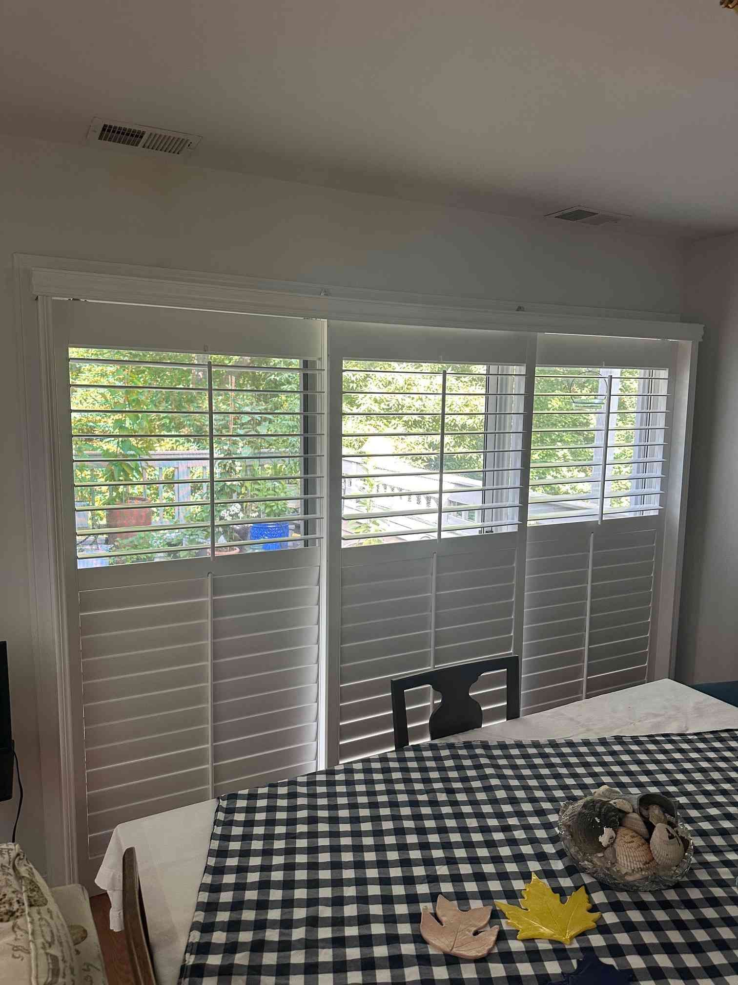 Dining room with checkered tablecloth, white shutters, and a small cat on the table near the window.