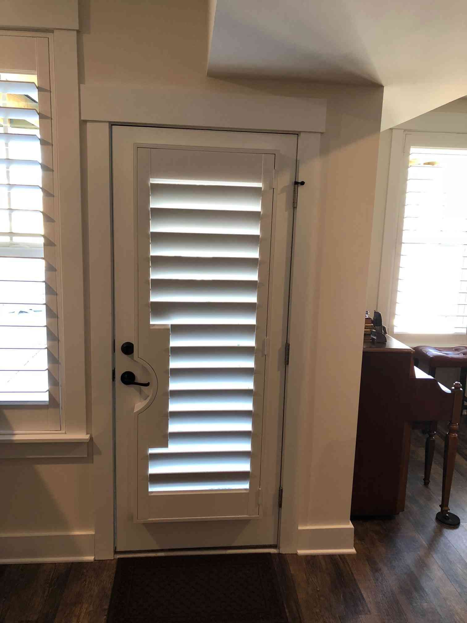White louvered door with black handle beside a bright window in a home interior