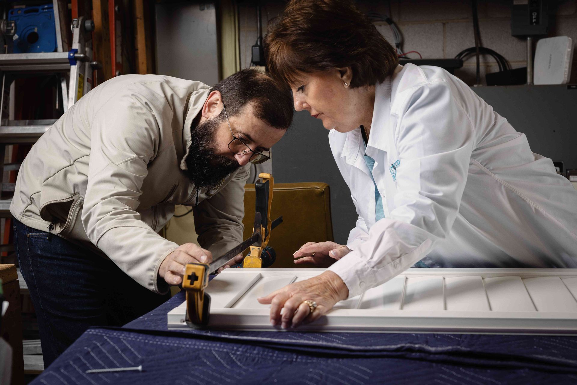 Two people in a workshop measuring a large panel with a tape measure and ruler.