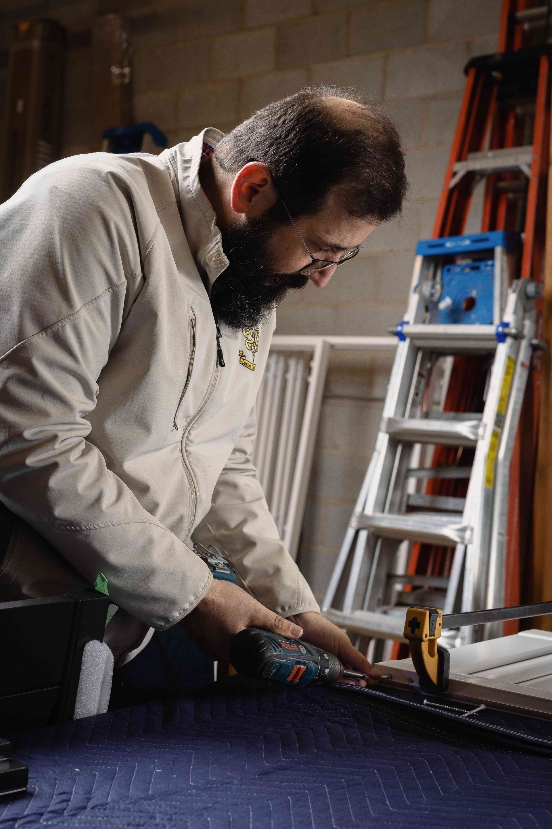 Man cutting a dark fabric panel with a utility knife in a workshop, ladder in background