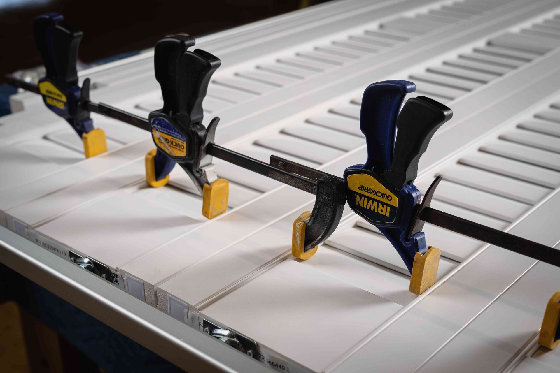 Three clamps holding a black rod on a white slatted workbench