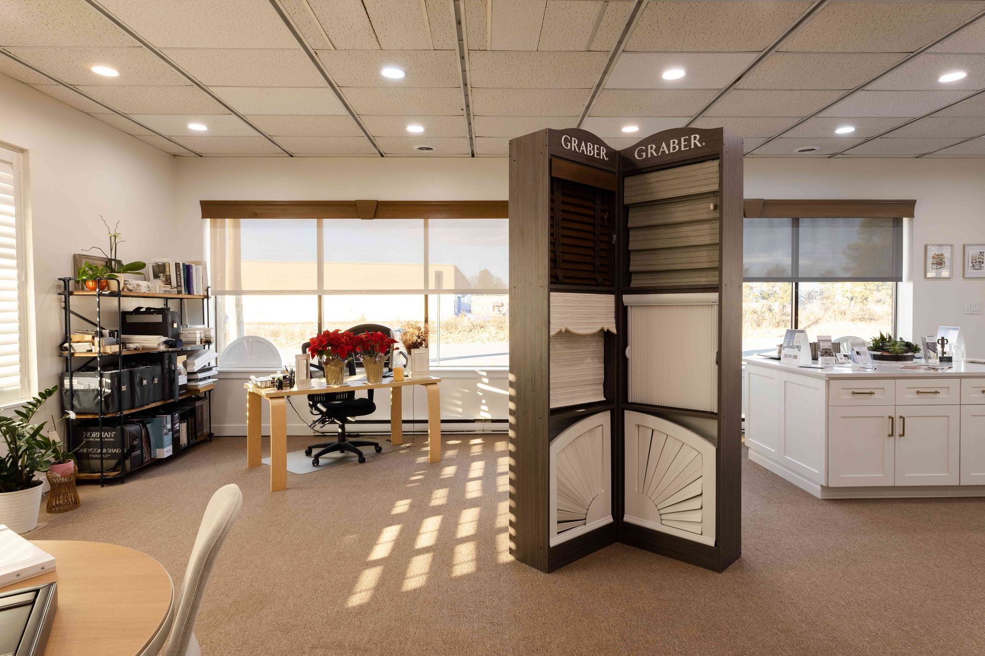 Bright office lobby with a display rack, desks, windows, and warm sunlight on the carpet.