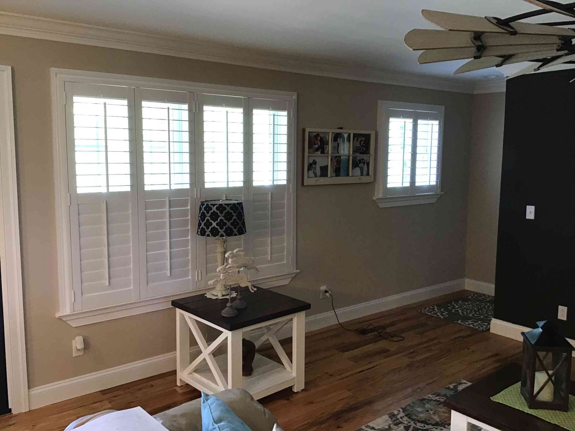 Living room with shuttered windows, hardwood floors, white side table, and ceiling fan