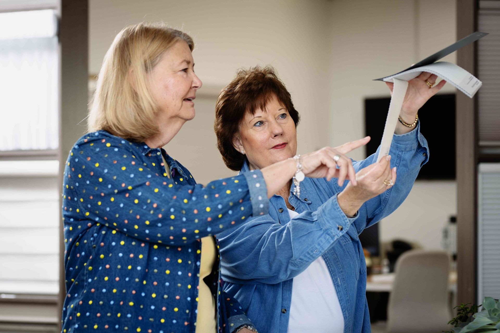 Two women in a room pointing and discussing a model airplane