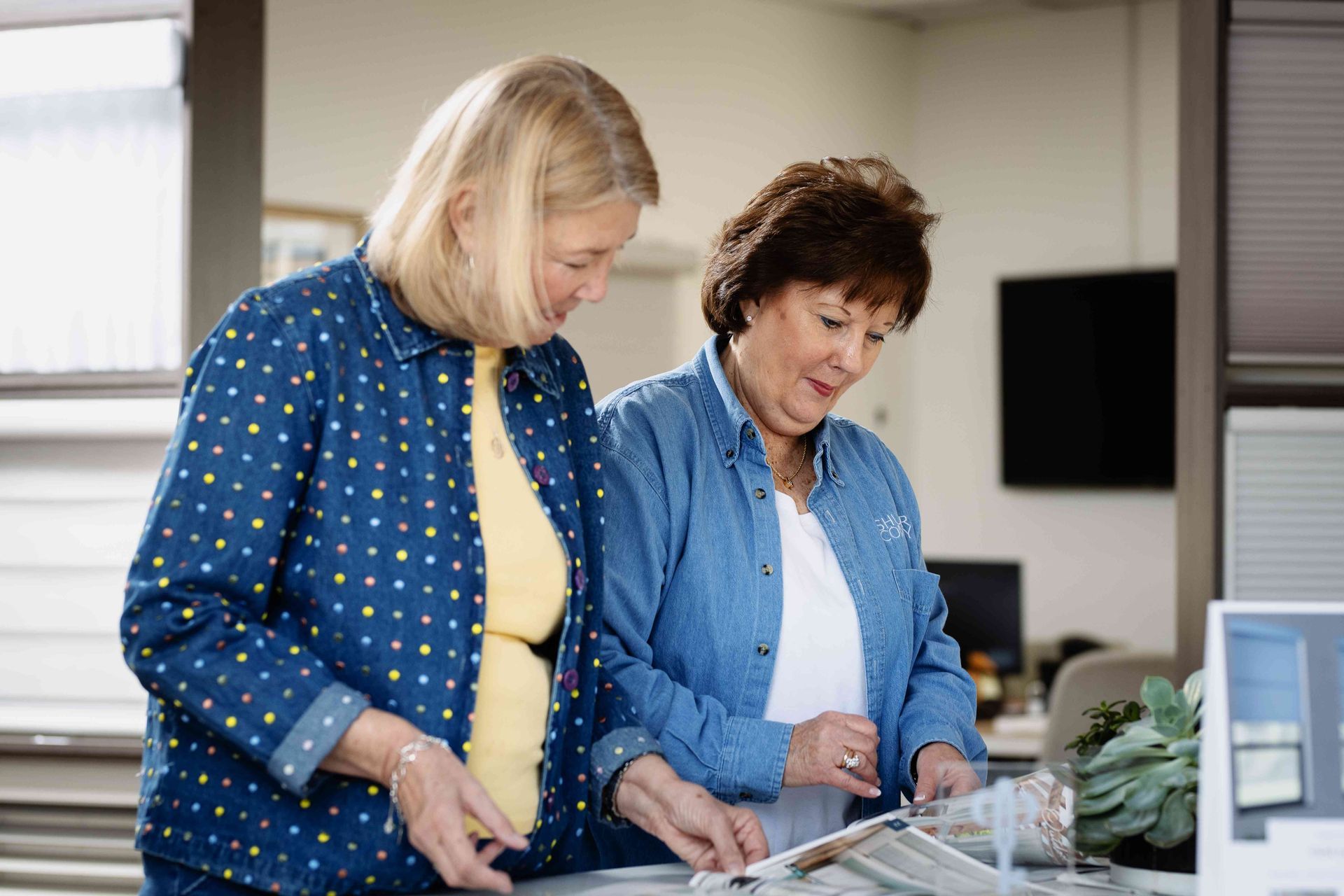 Two women in a kitchen, preparing food and looking down at a counter with dishes.