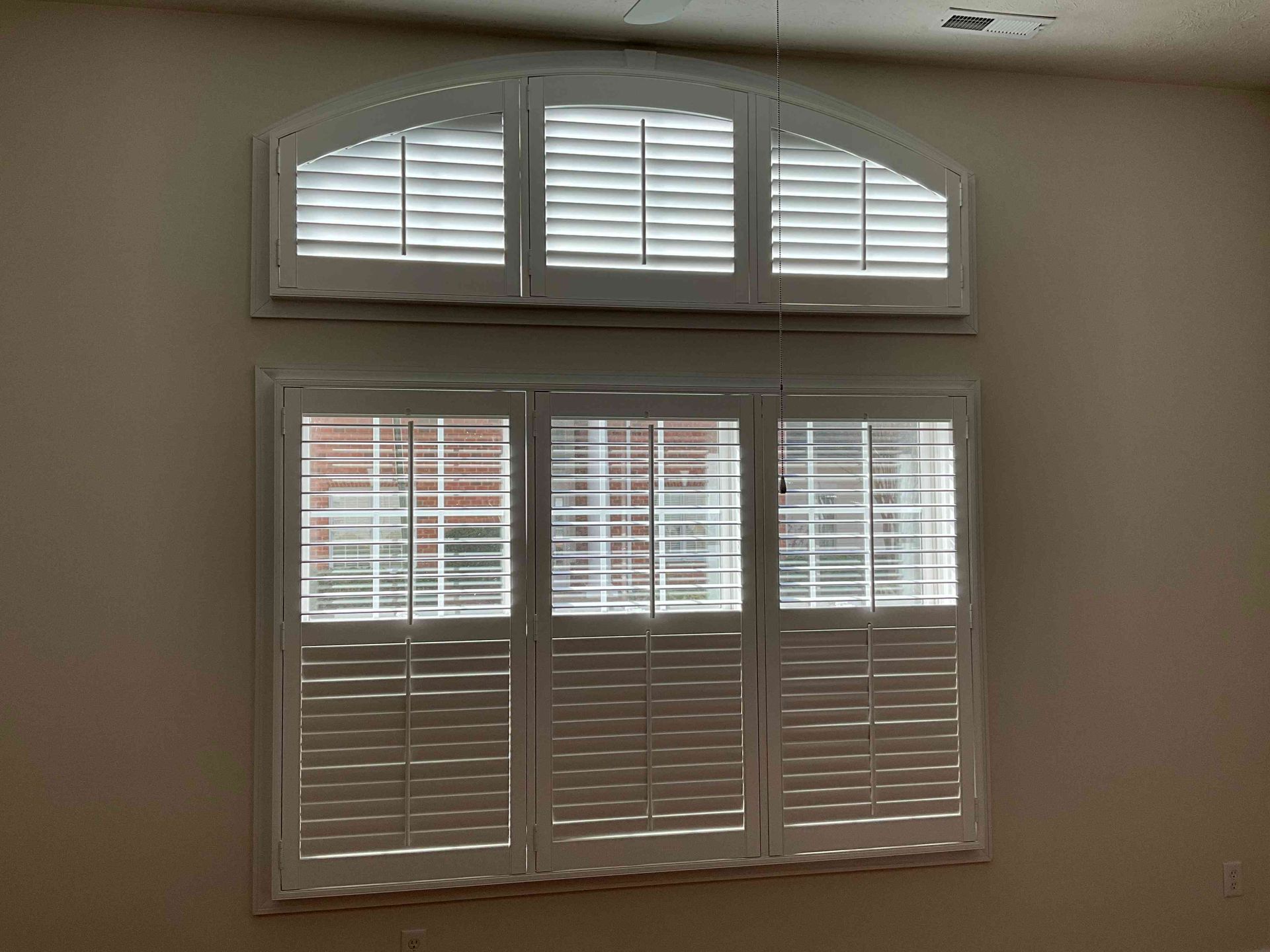 White plantation shutters covering a large arched window in a beige room