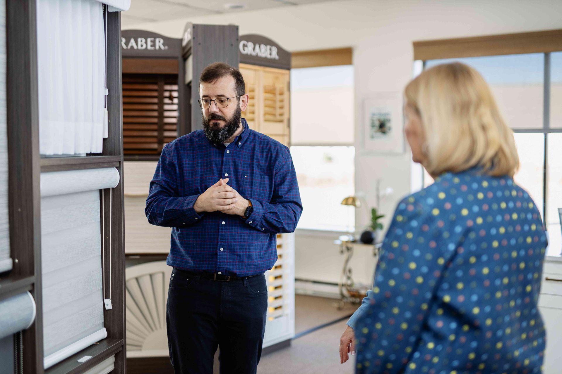 Two people talking in a bright room with storage bins and a window.