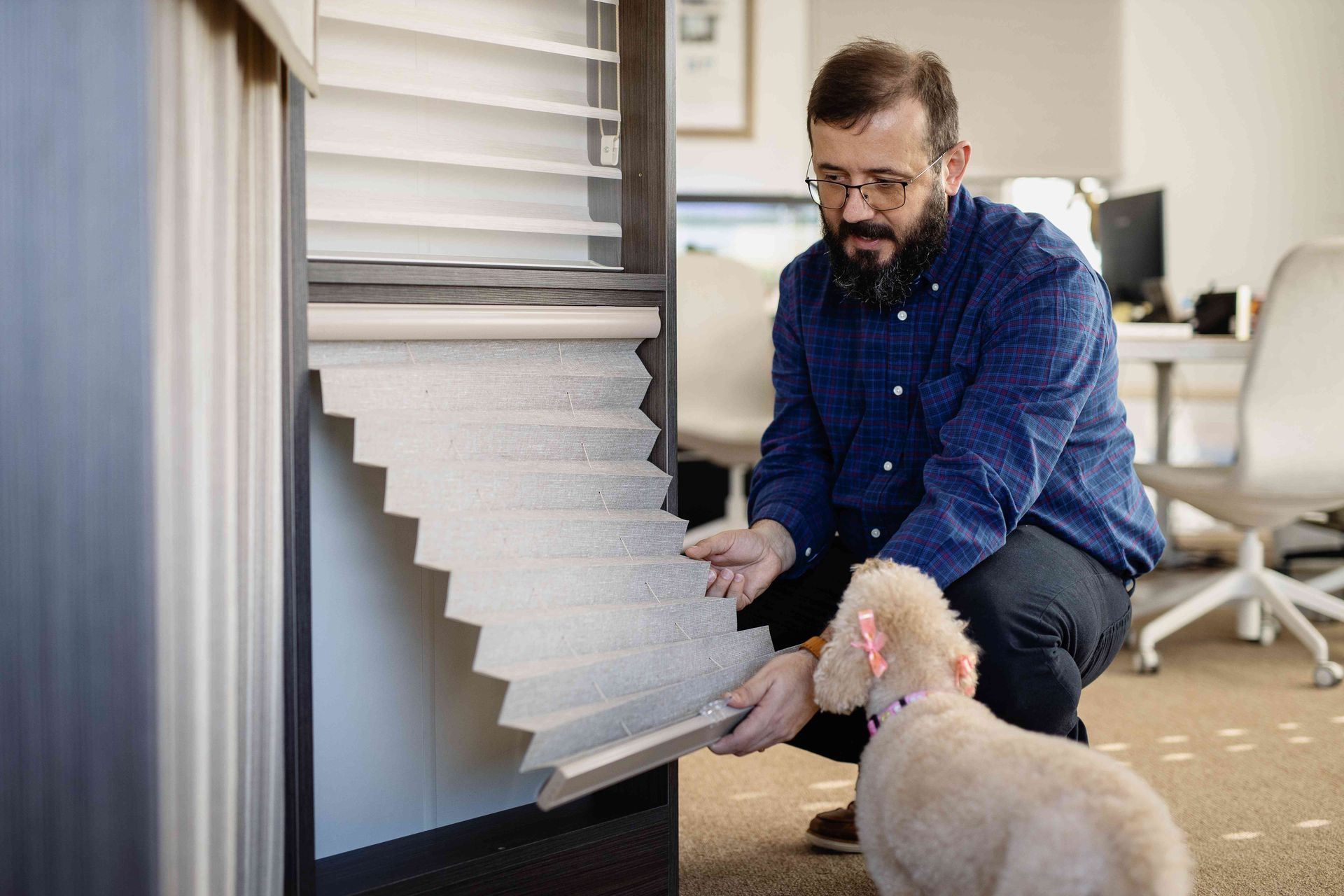 Man adjusting window blinds while a white dog watches indoors