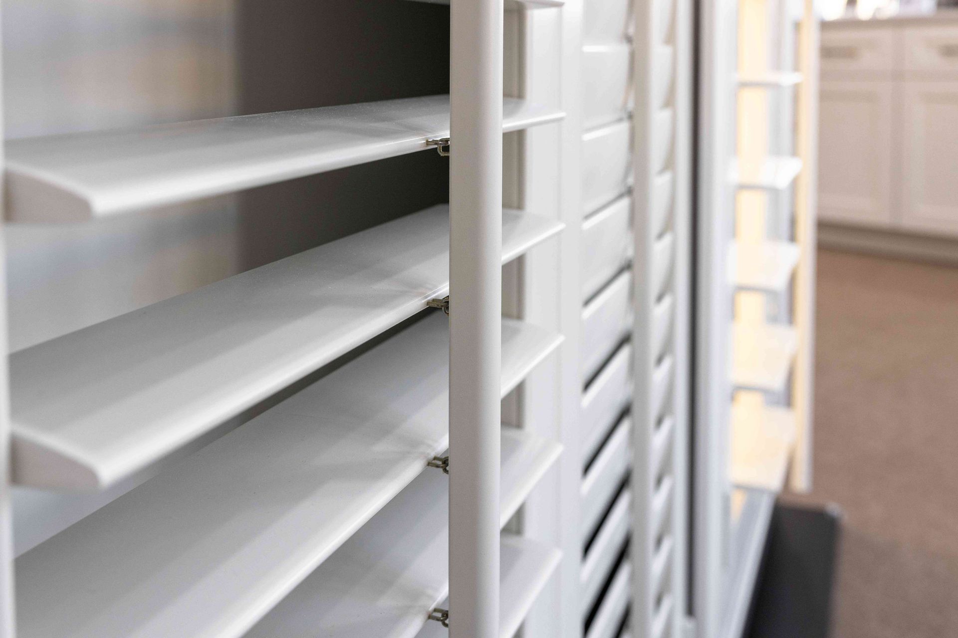 Close-up of white window blinds with slats partially open, showing a room beyond.