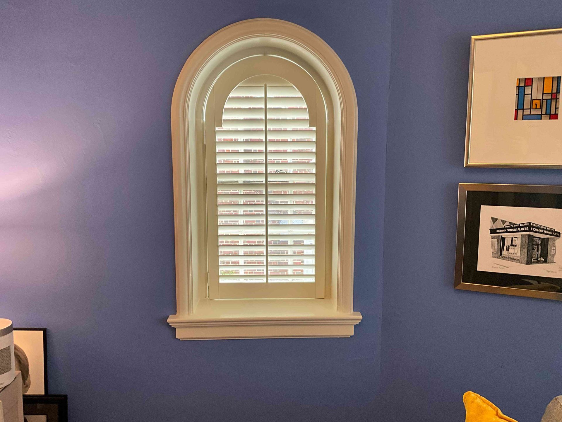 Blue bedroom wall with a centered arched window and framed artwork on the right