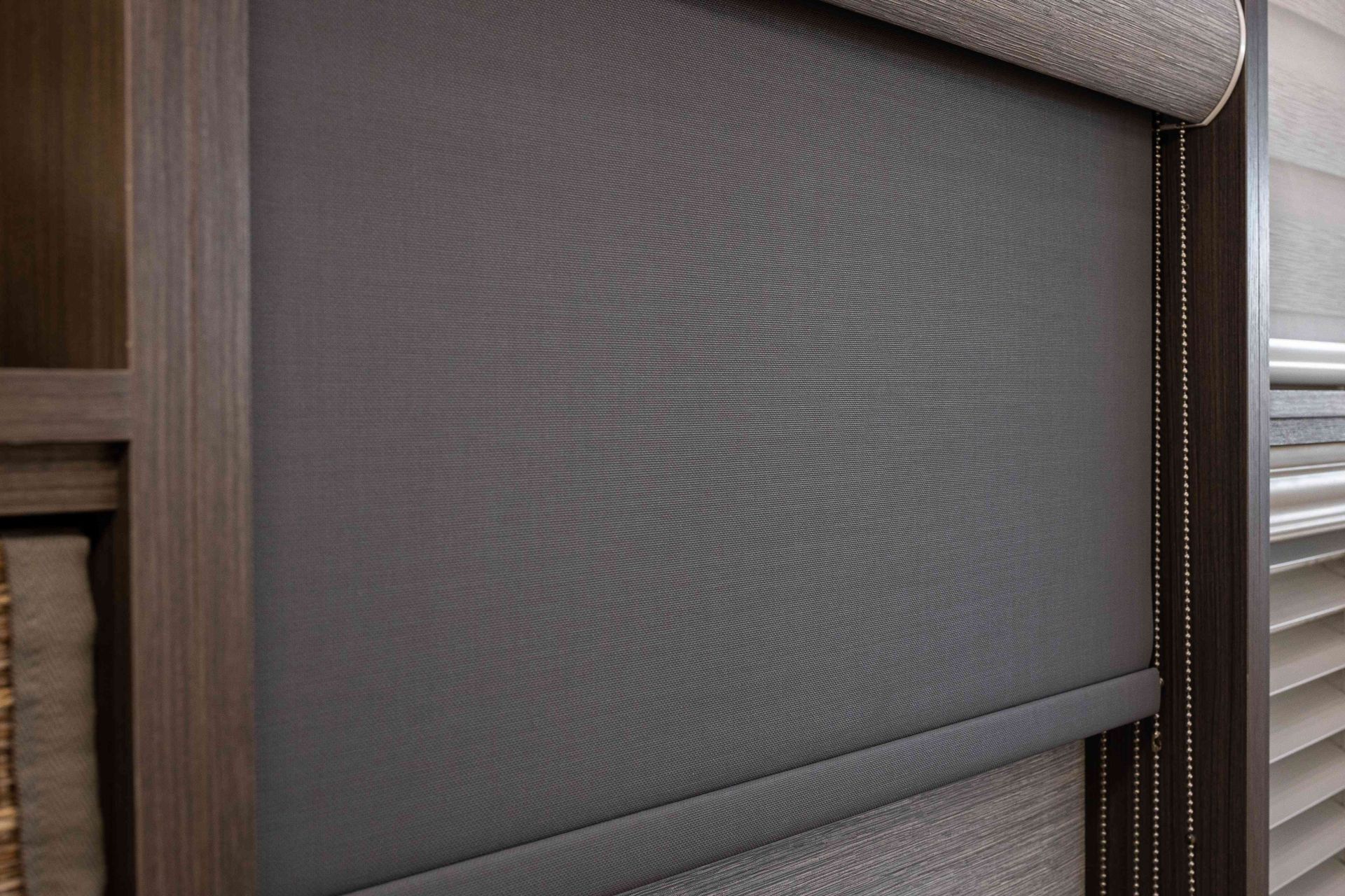 Close-up of a gray roller window shade with a textured pattern, mounted in a wooden frame.