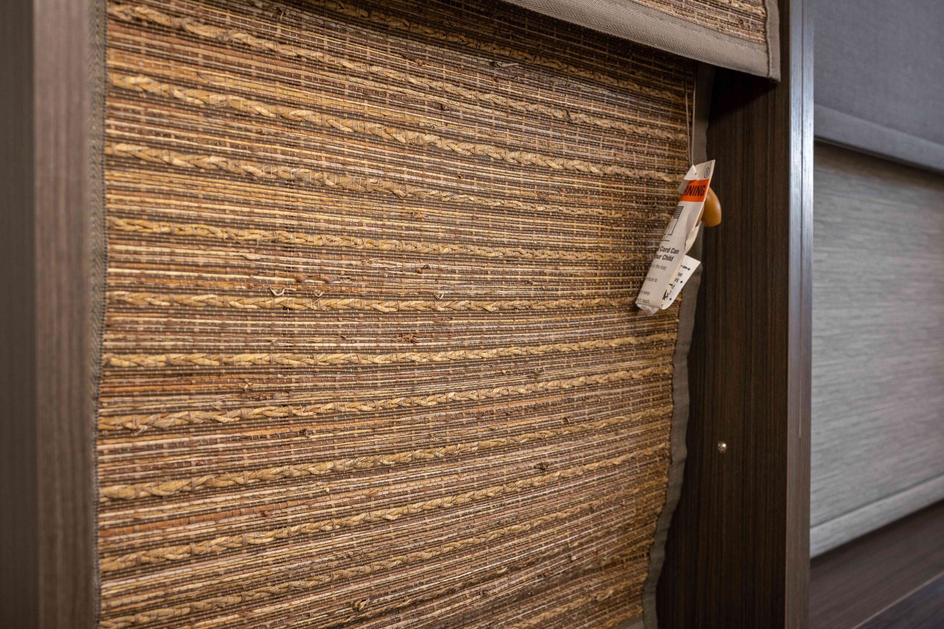 Woven window blind in a hallway, with a hanging safety tag on the right edge.