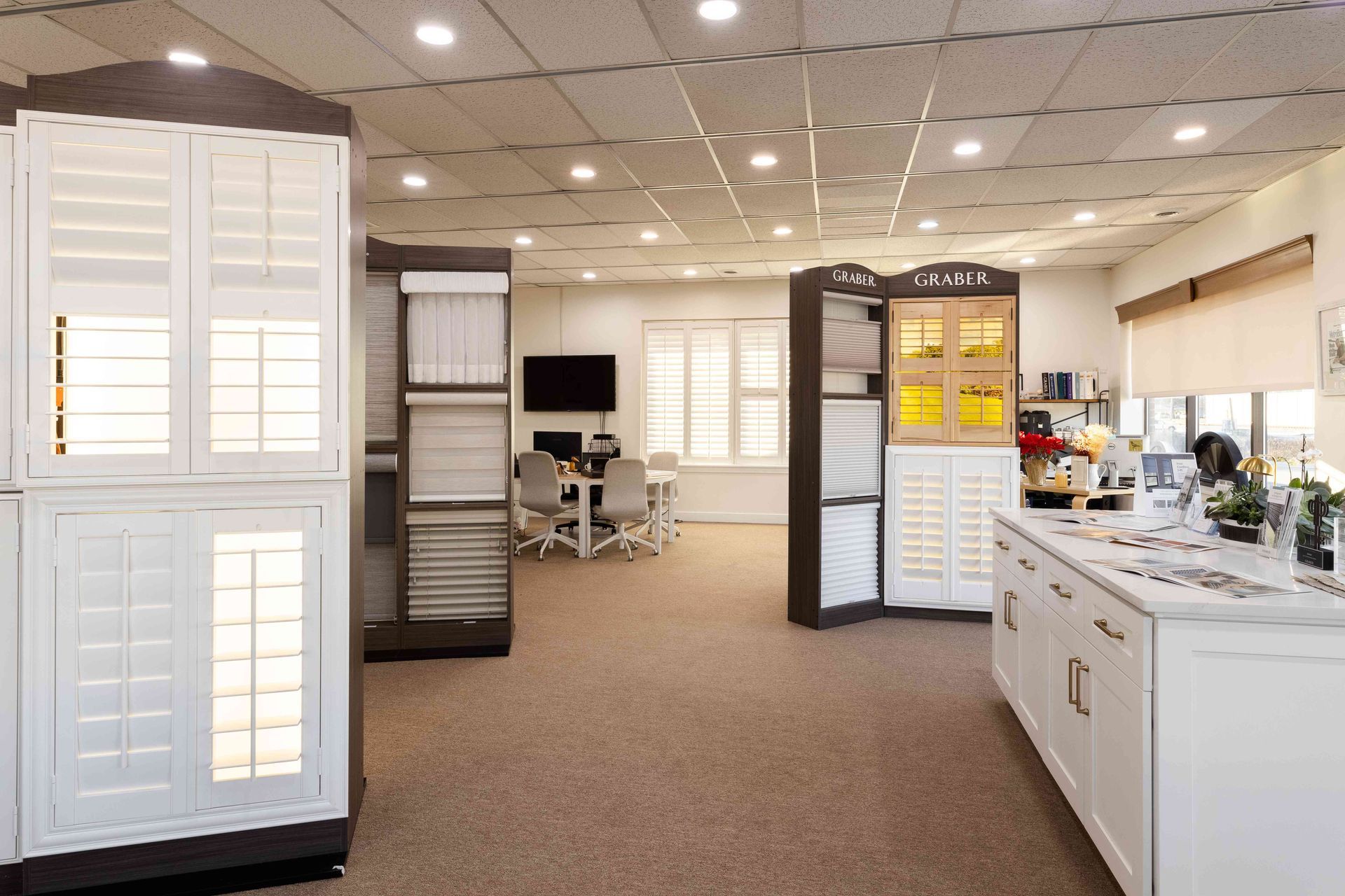 Bright showroom with cabinets, display panels, and a desk under recessed lighting