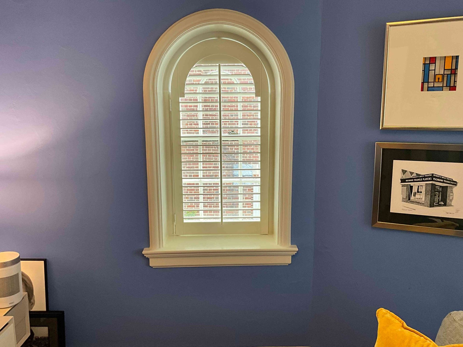 Blue room with arched window, blinds, and framed artwork on the wall