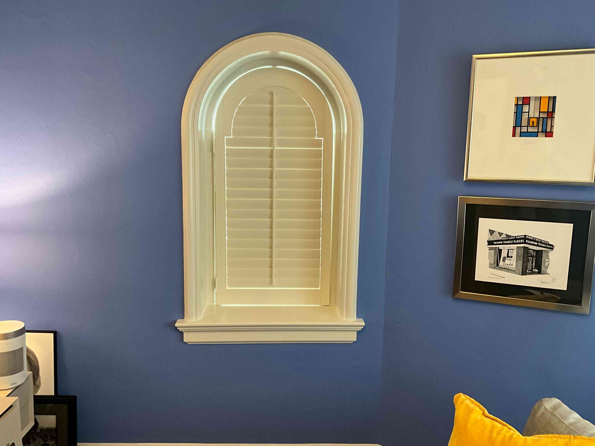 Blue wall with arched window and two framed pictures above a gray sofa with yellow pillow