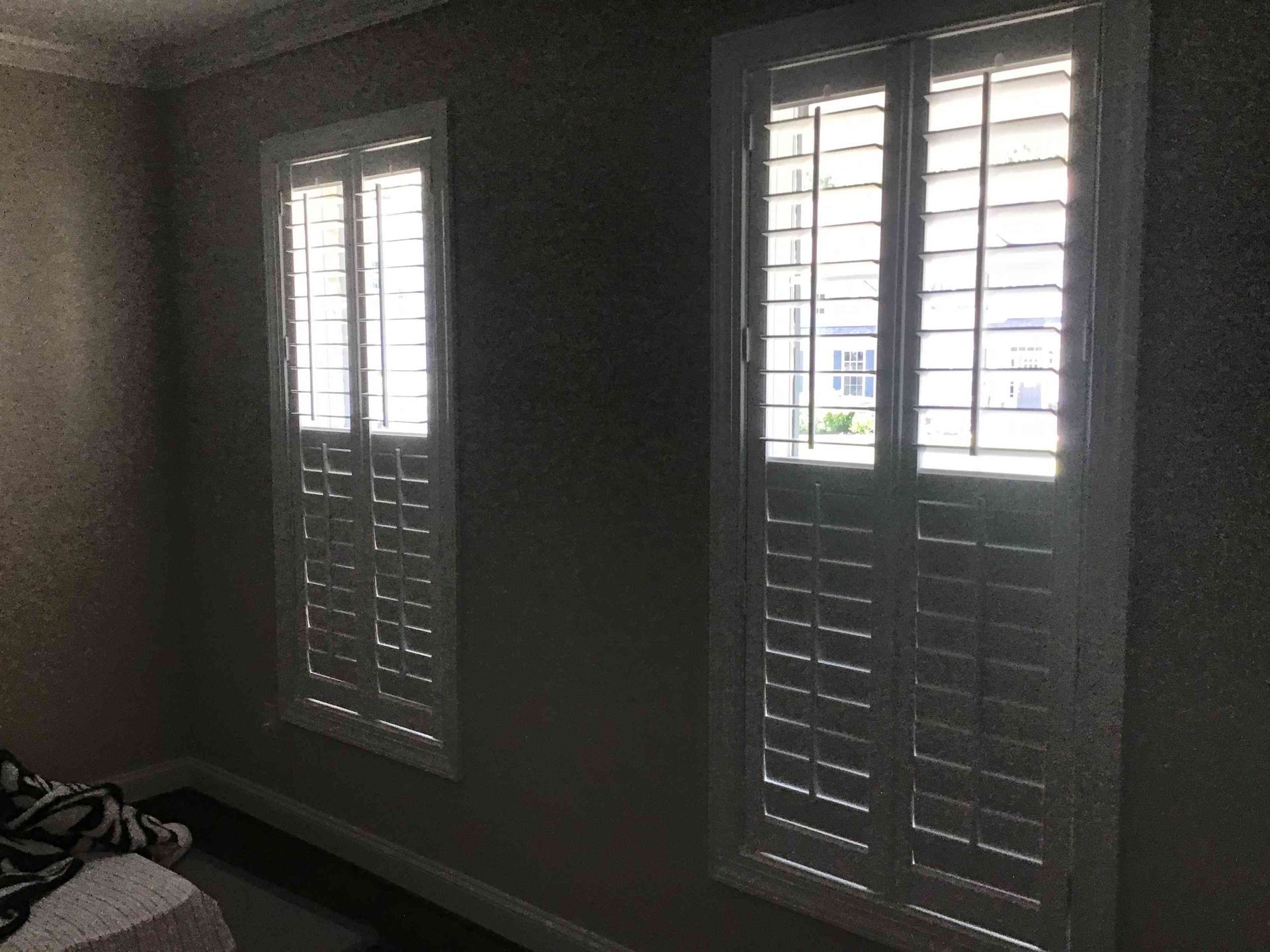 Dim room with two white shuttered windows letting in bright daylight.