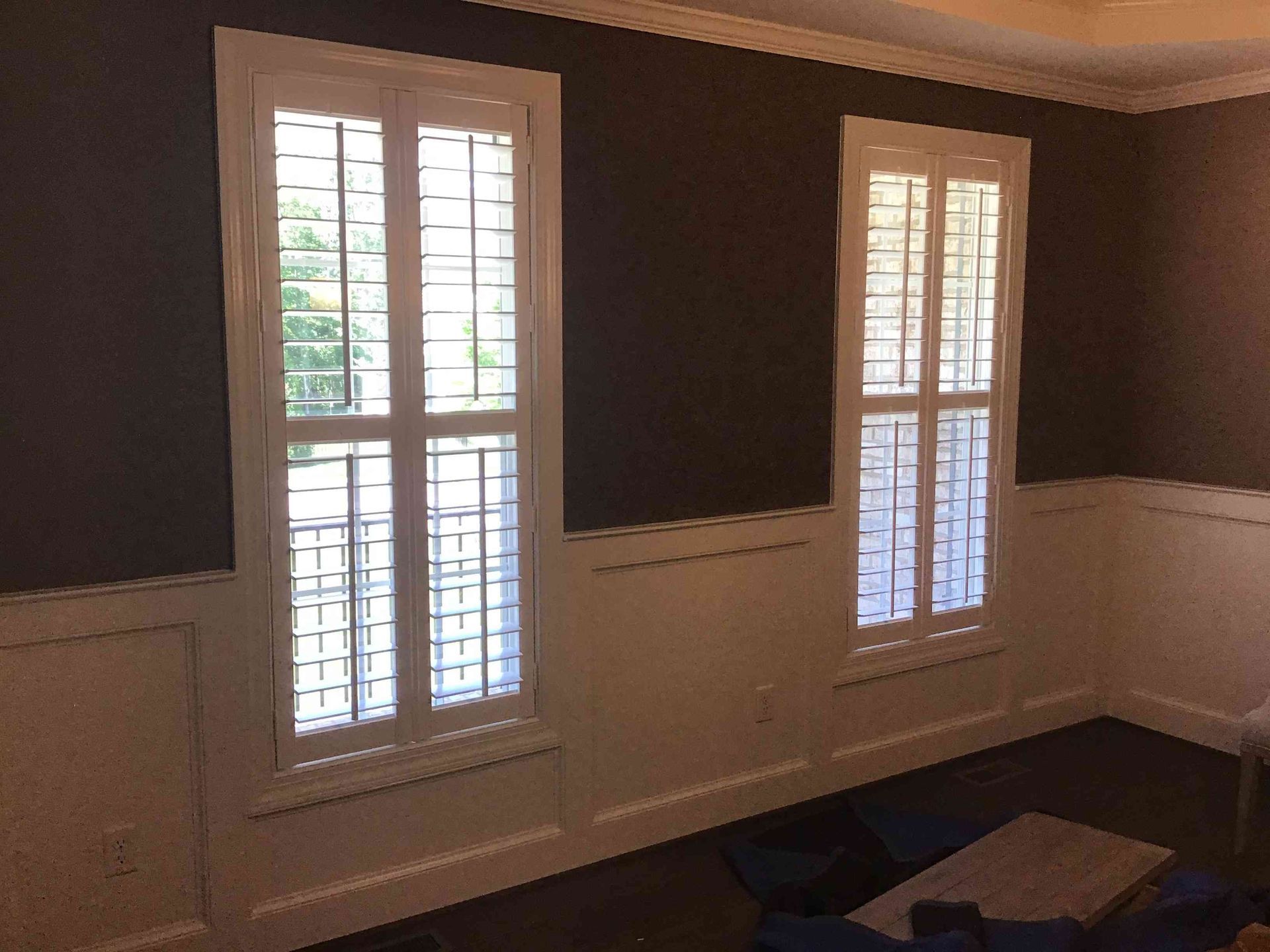 Empty room with dark walls, white wainscoting, and two tall windows with shutters.