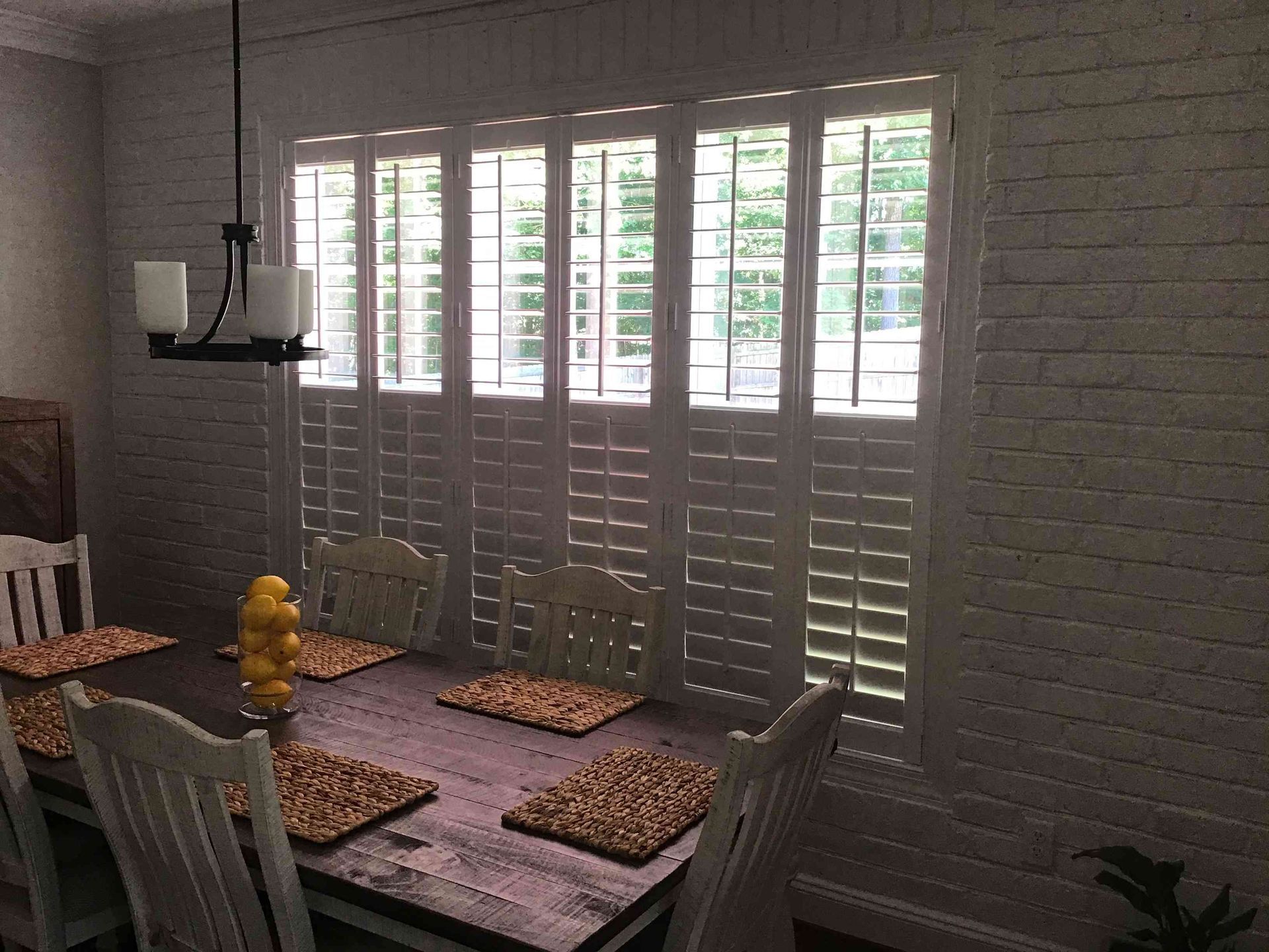 Dining room with white shutters, glass table set for four, and a yellow flower vase.