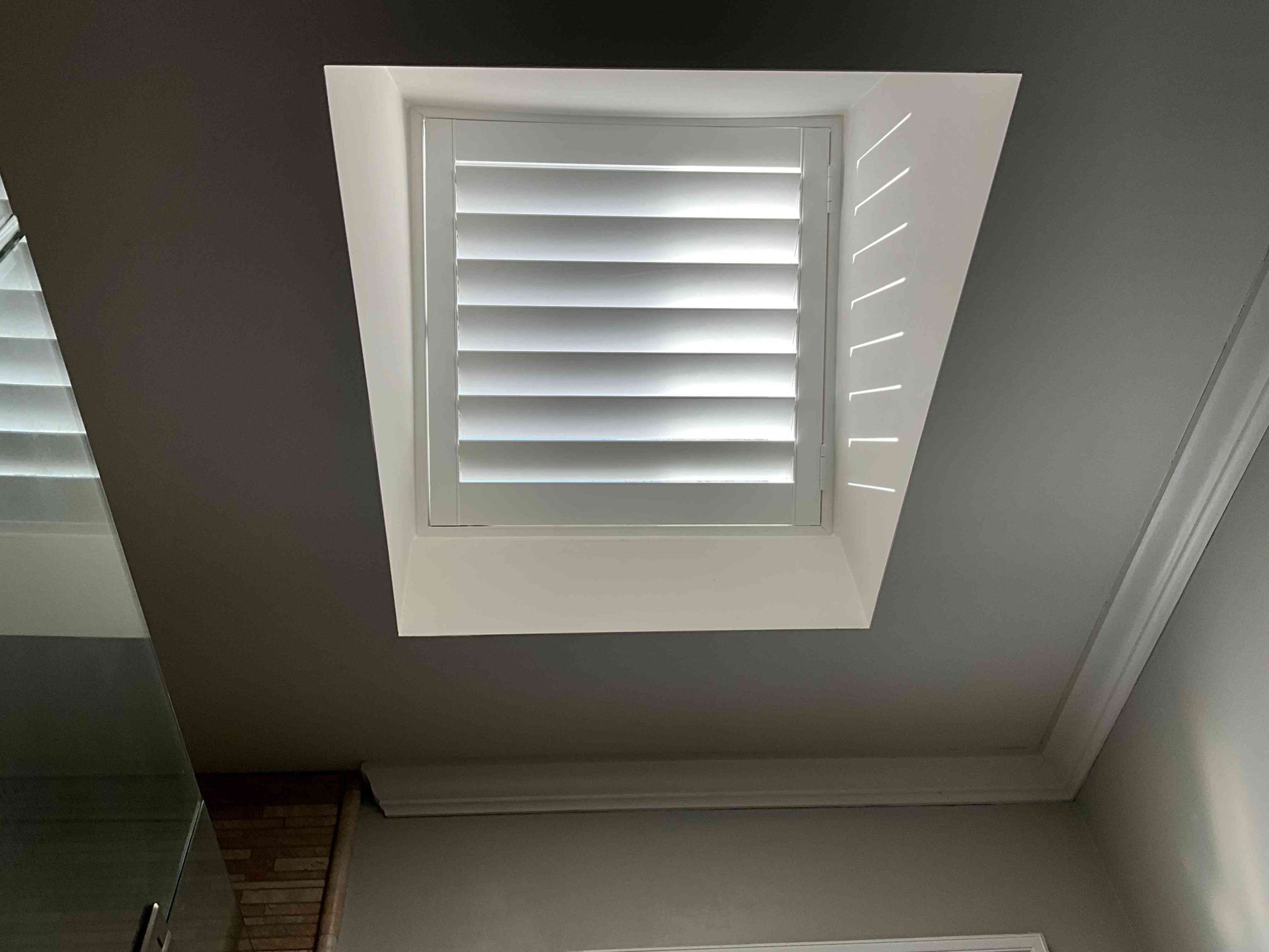 White louvered skylight set in a slanted ceiling, letting in daylight.