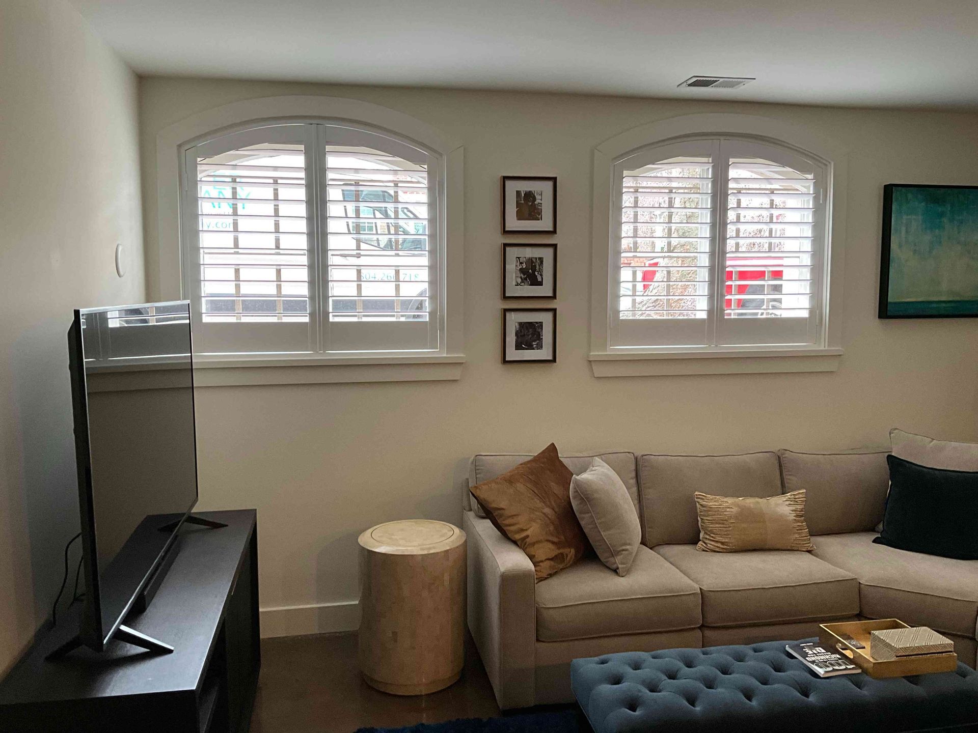 Cozy living room with sofa, ottoman, TV, and arched windows letting in daylight