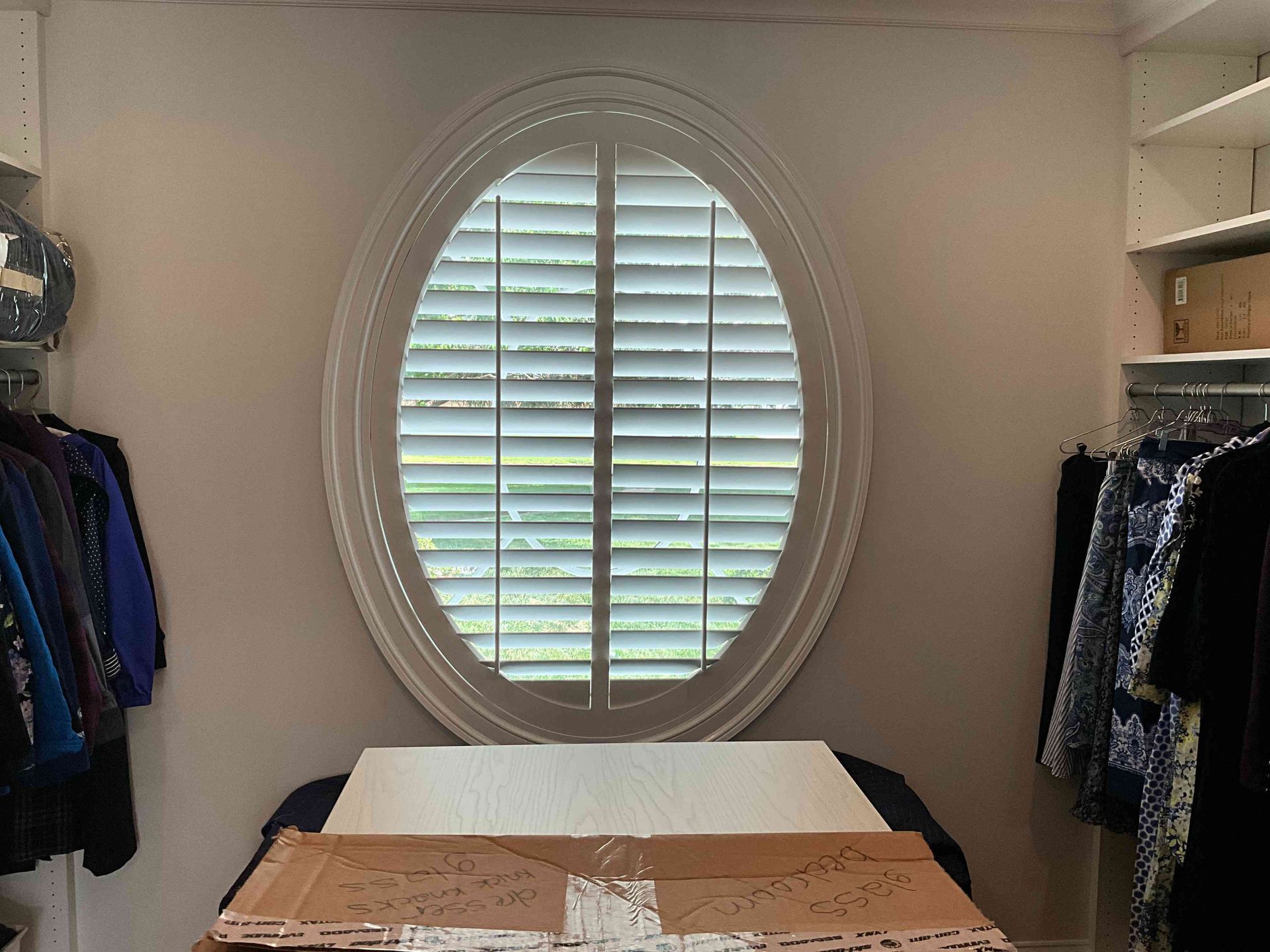 Empty bedroom with an oval window, closet clothes on both sides, and a bed or table in the foreground