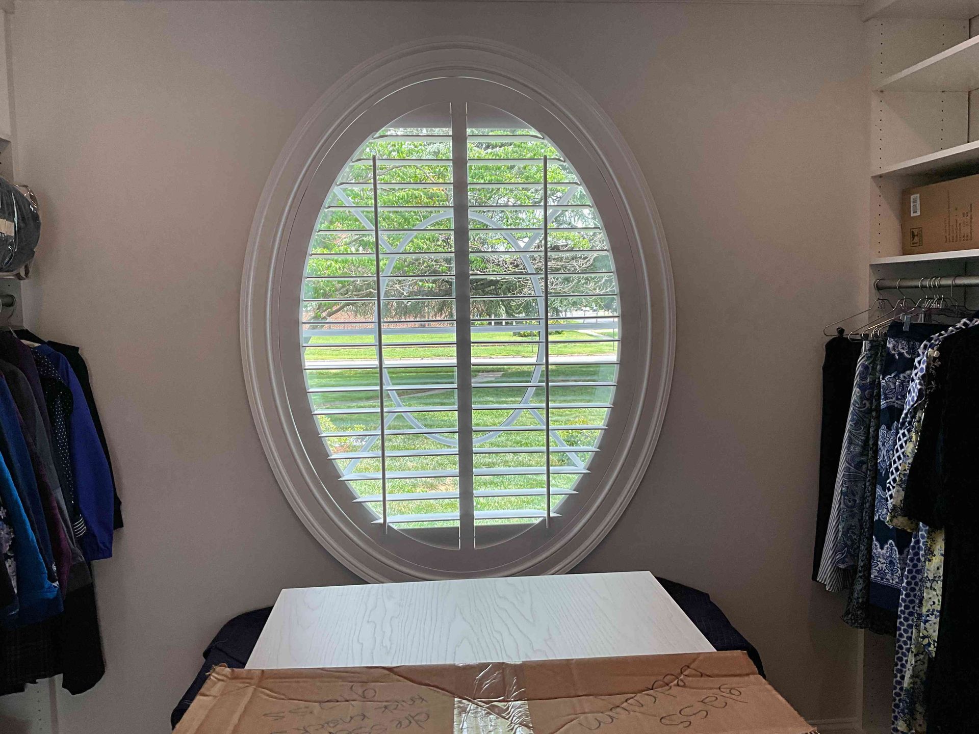 Bedroom with an oval window, a bed, and clothes hanging on both sides