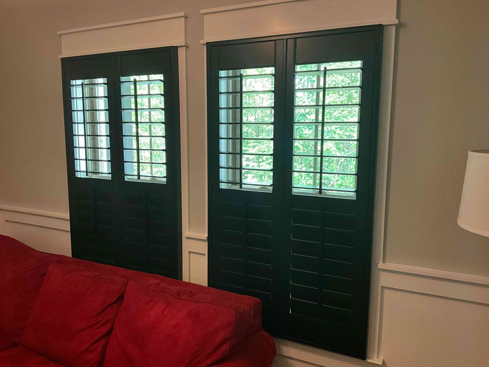 Living room wall with dark green window shutters above a red couch and white wainscoting
