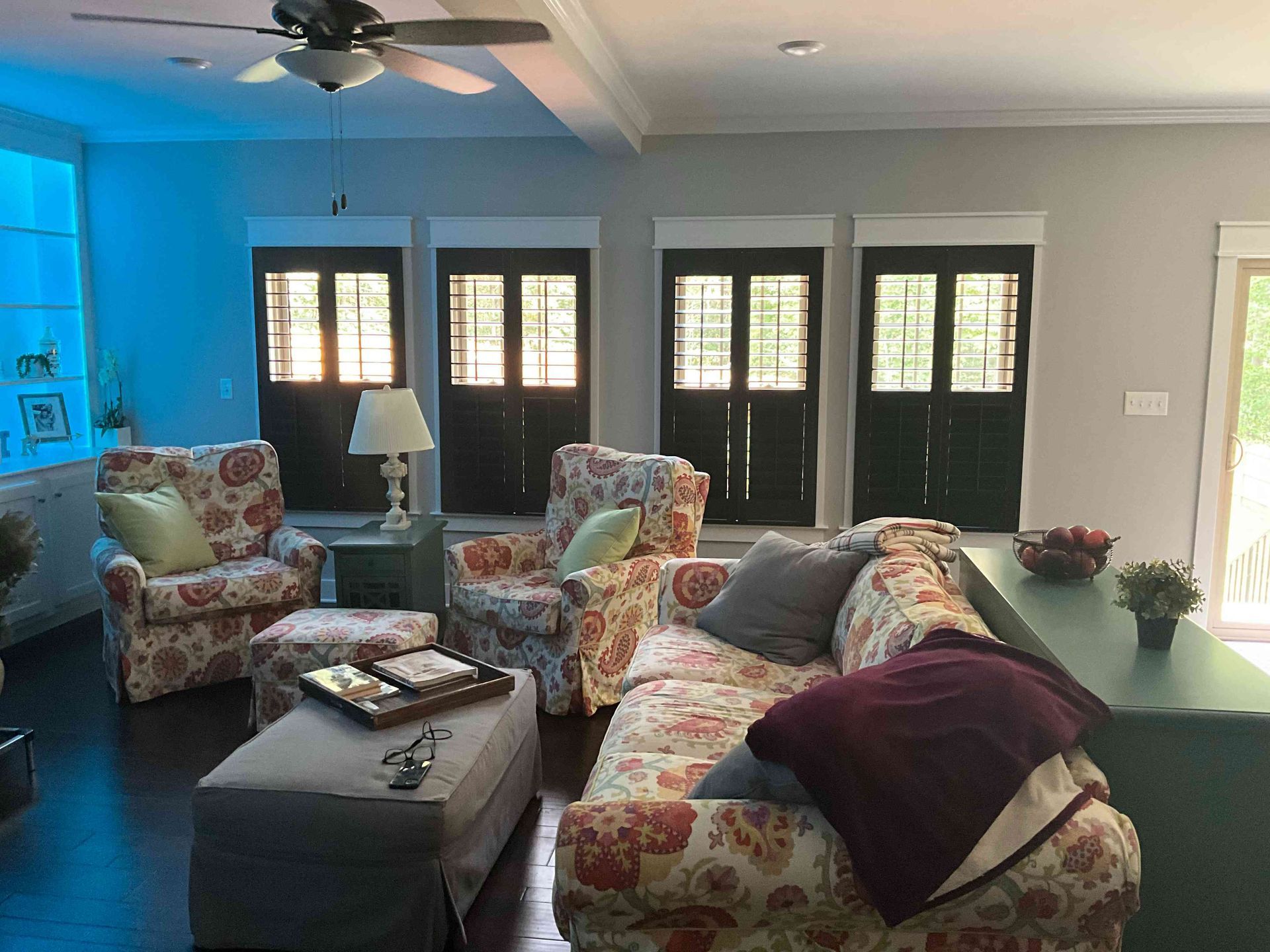 Bright living room with floral chairs, gray ottoman, blue accent wall, and dark French doors.