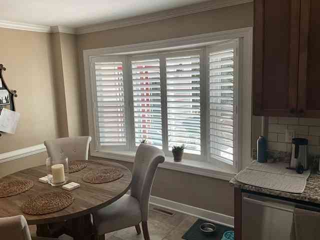 Dining nook with round table, upholstered chairs, and bay window with white shutters
