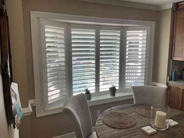 Dining area with round table, two chairs, and bay window with white shutters￼