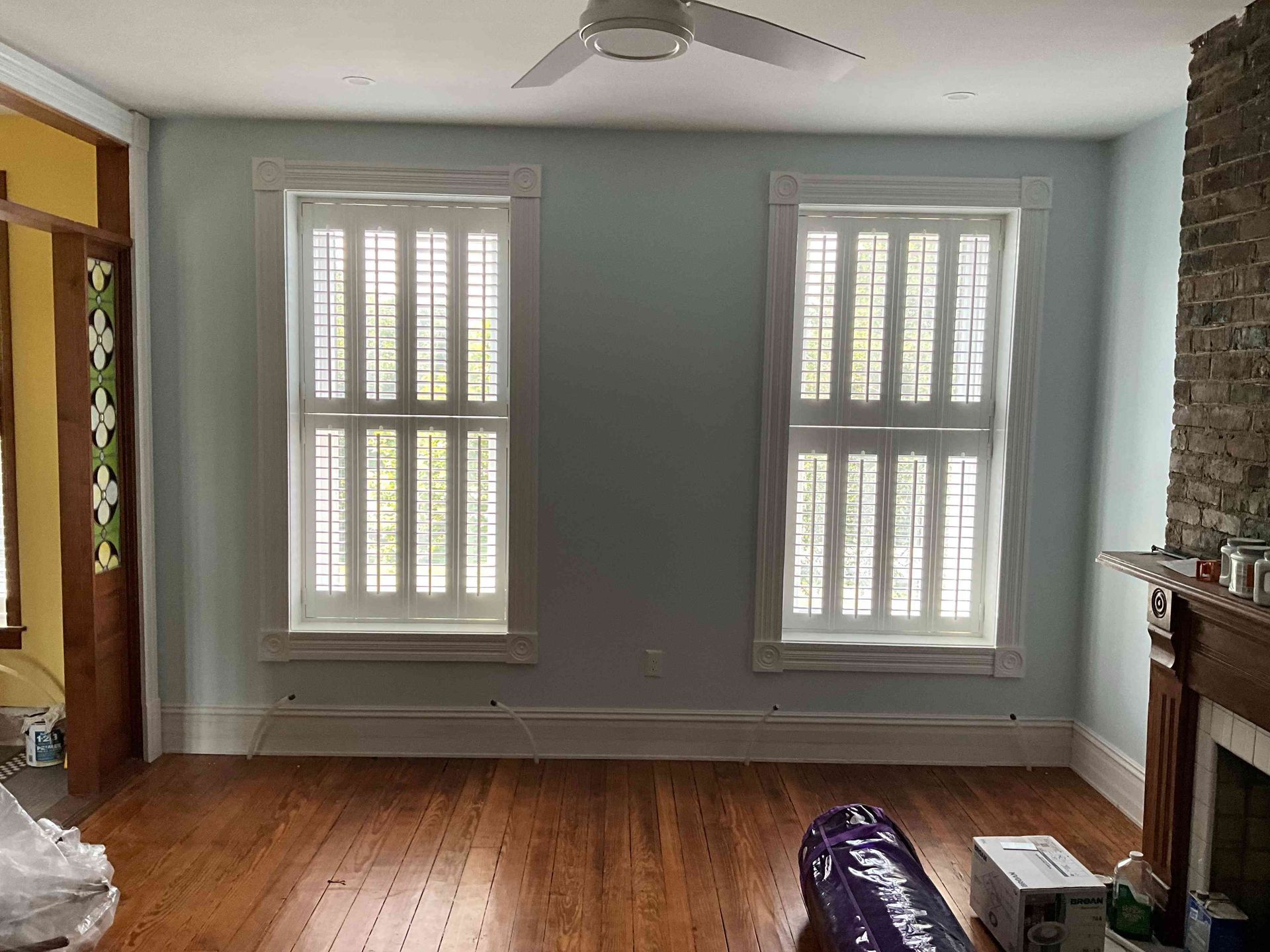 Empty living room with two windows, pale walls, hardwood floor, and a fireplace on the right.