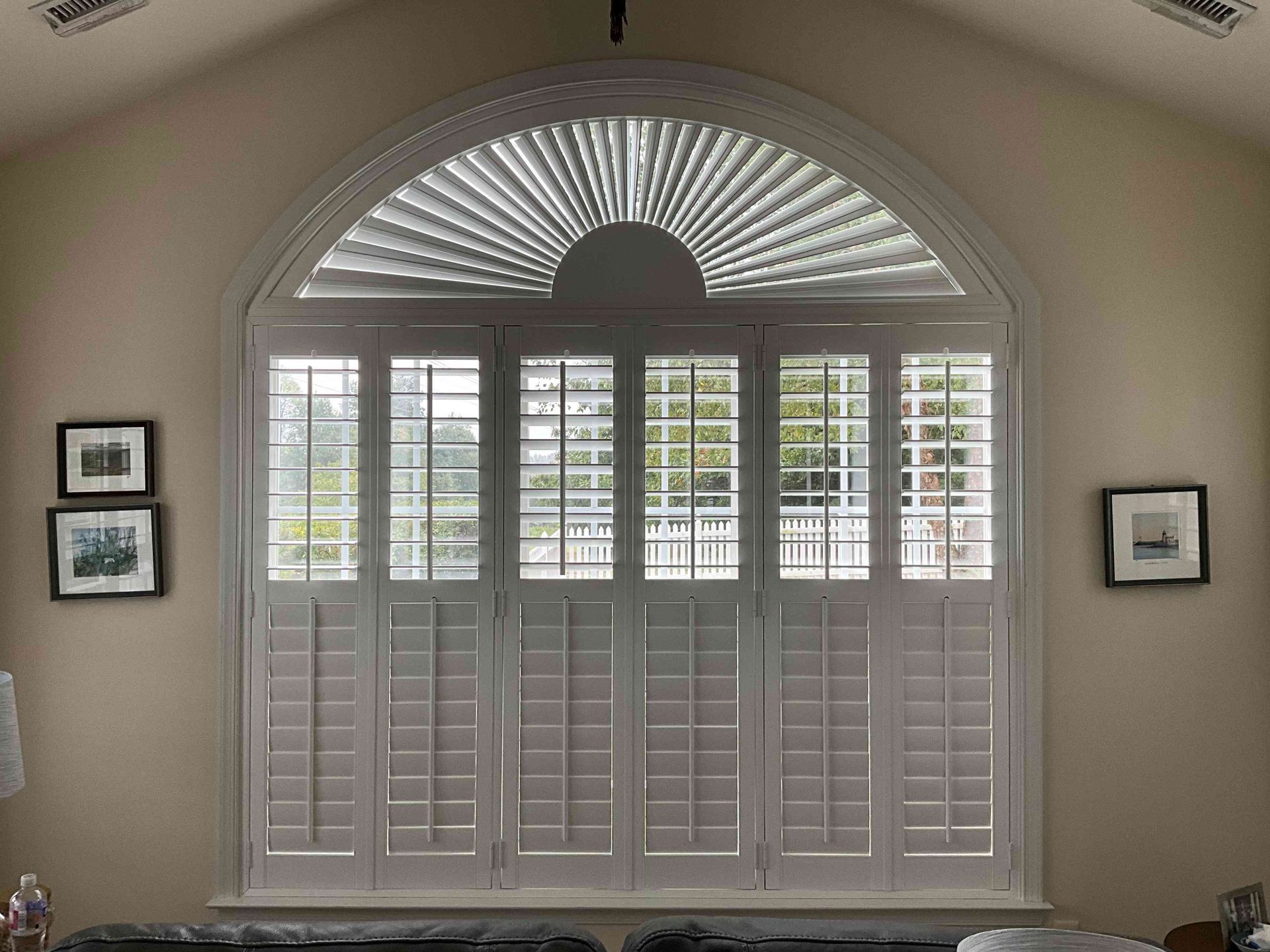 White plantation shutters with a fanlight window in a softly lit arched alcove, flanked by framed pictures.