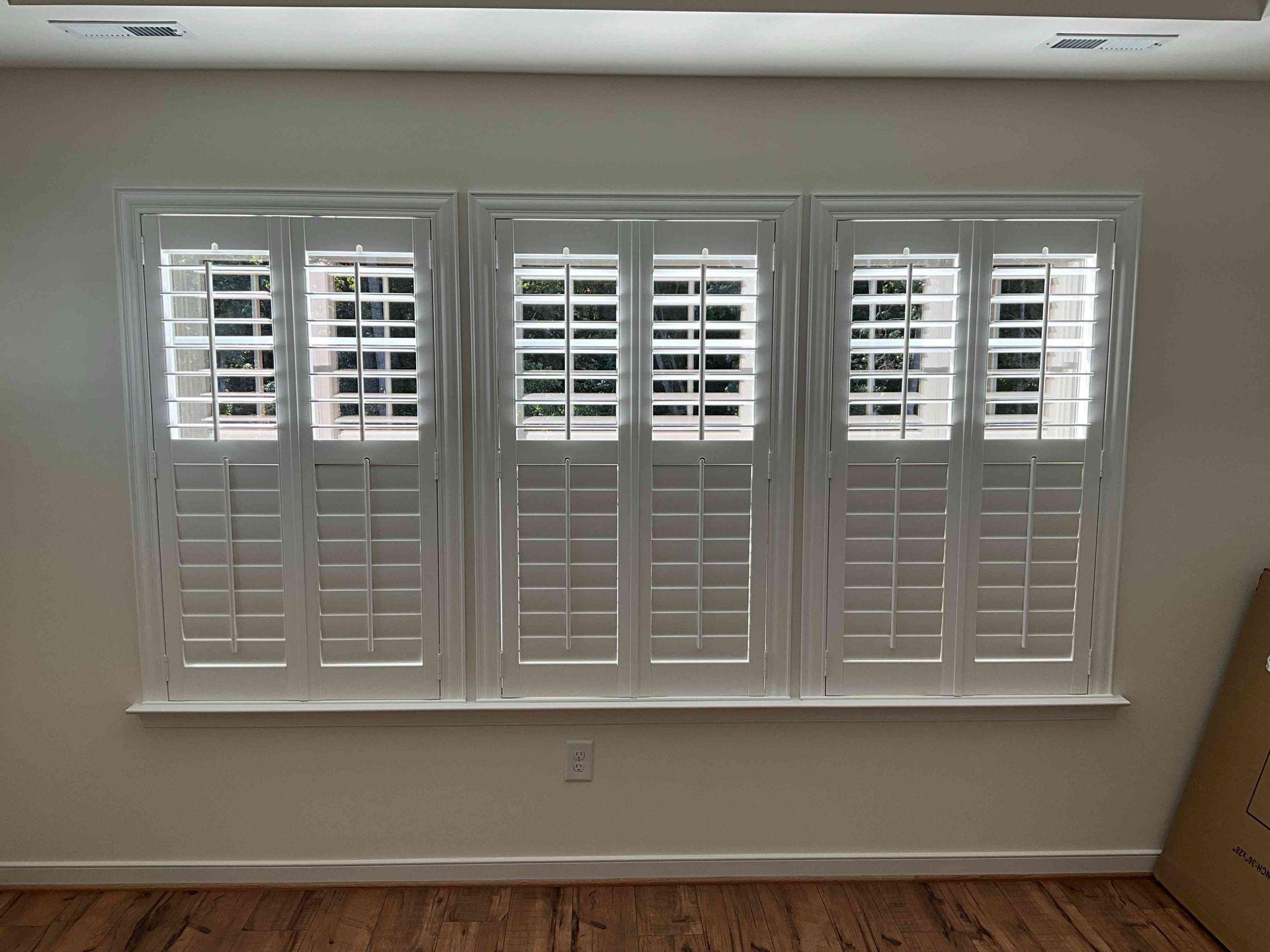 Living room wall with three white shuttered windows and a small wall outlet beneath them.