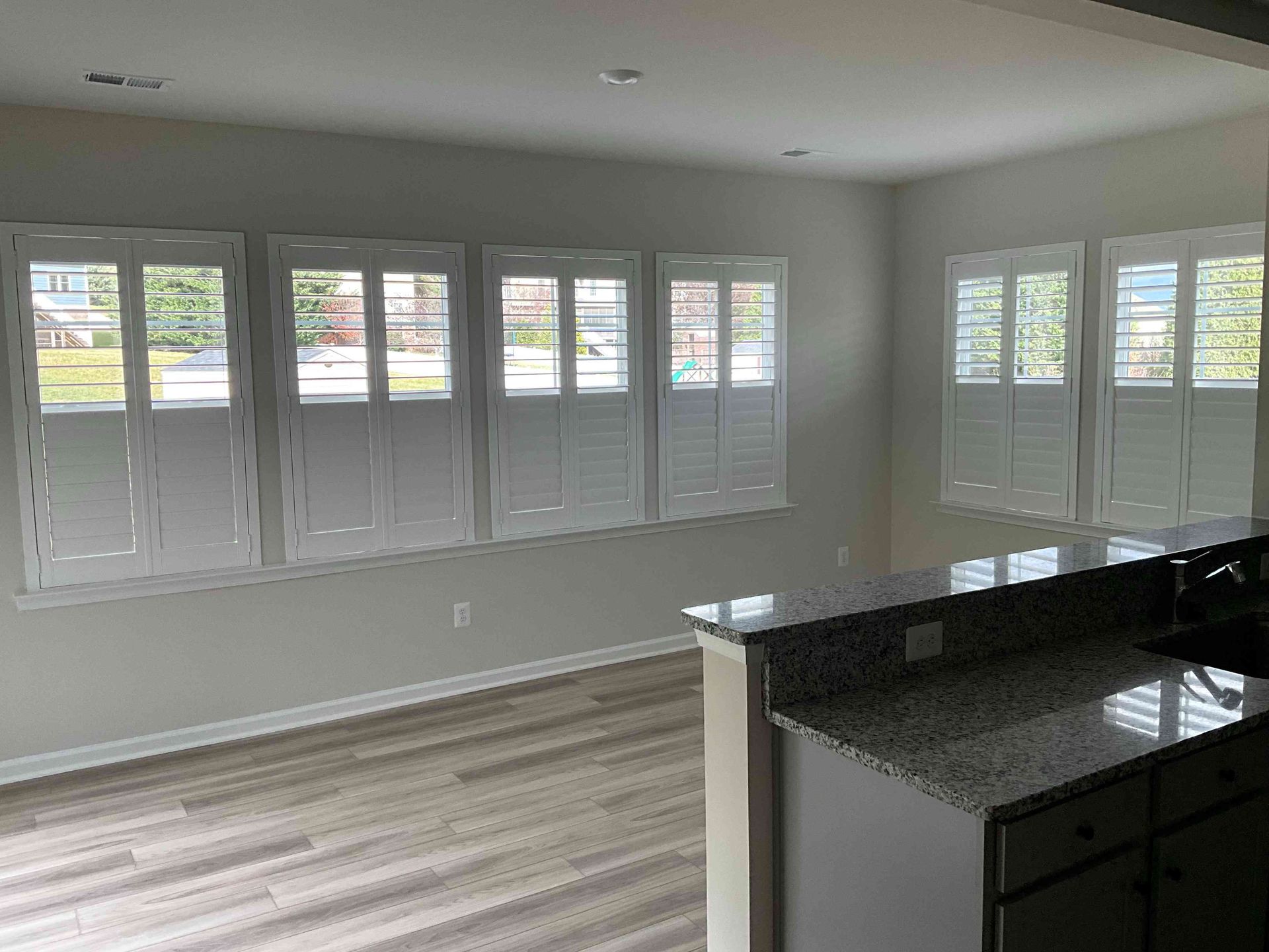 Bright empty room with large windows, gray walls, wood floors, and a kitchen island with dark countertops