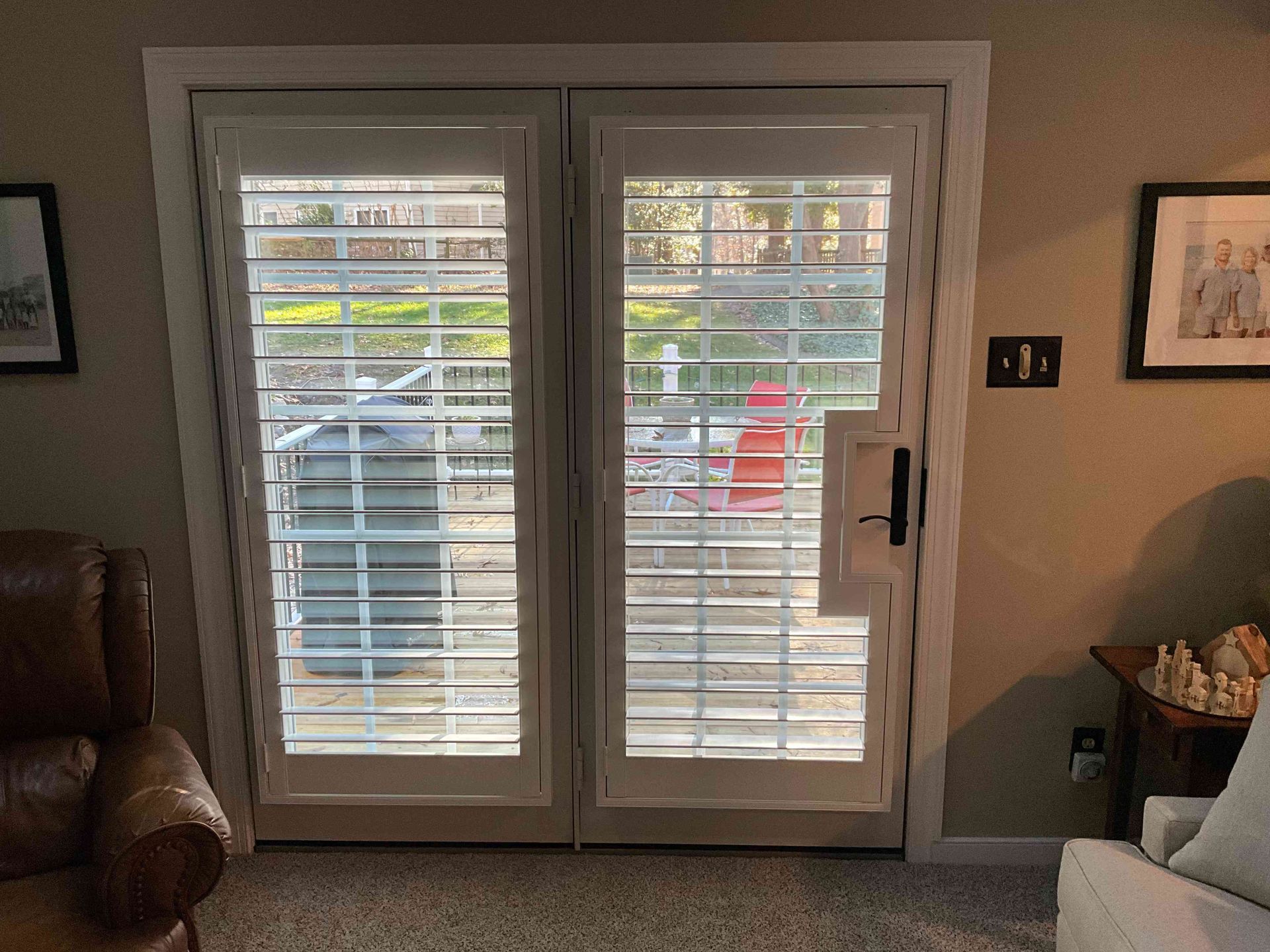 Sliding glass doors with white blinds in a living room, showing a porch and parked car outside.