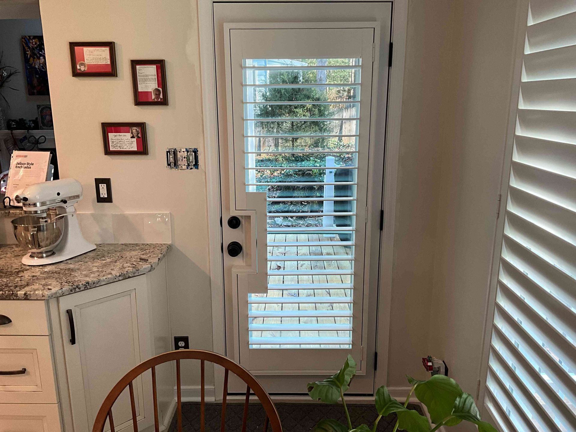 Kitchen with countertop, stand mixer, wall decor, and a glass door with white blinds overlooking a patio.