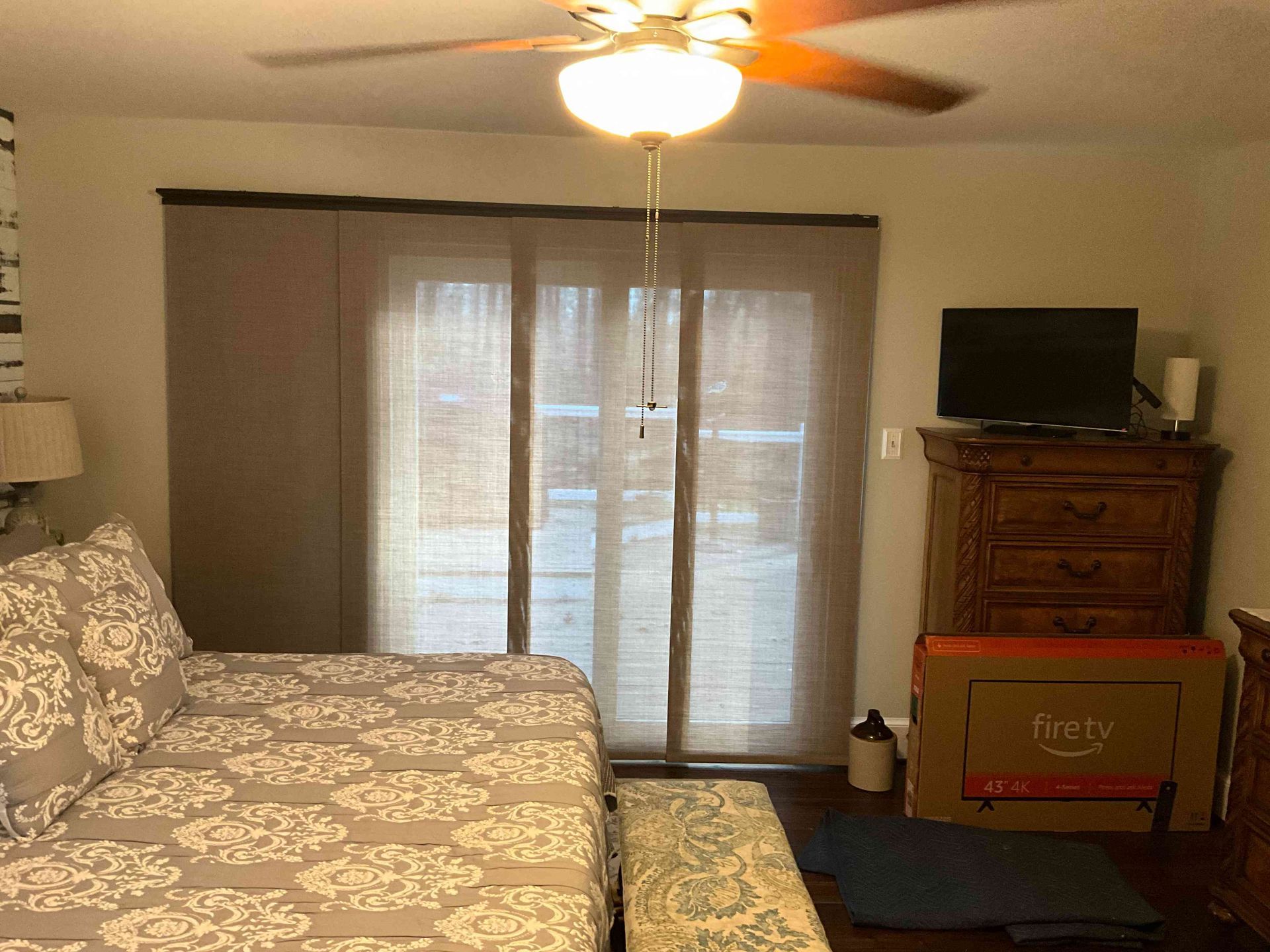 Bedroom with bed, ceiling fan, dresser, TV, and sliding glass doors with curtains