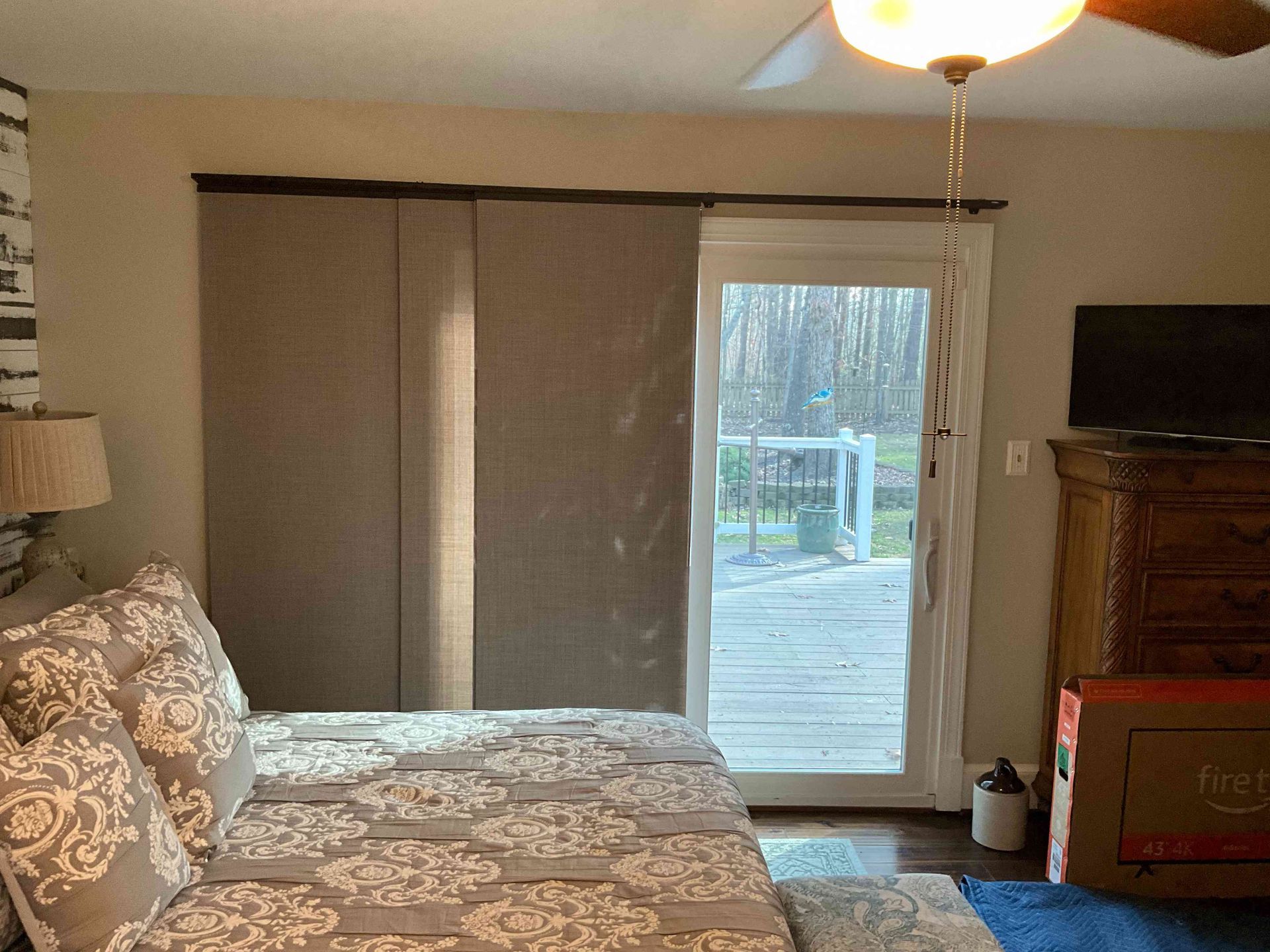 Bedroom with patterned bedspread, closed blinds, and a sliding glass door opening to a deck.