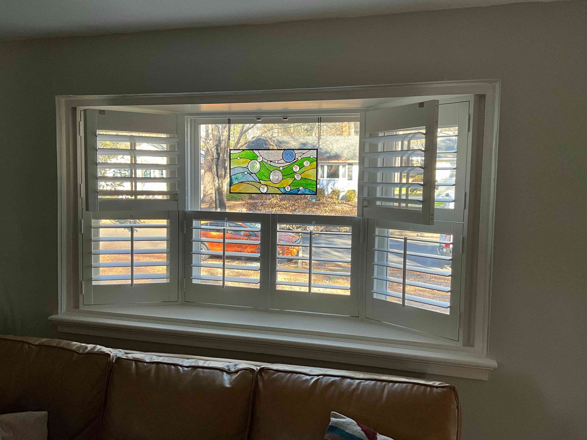 Bay window with white shutters and a colorful stained-glass panel above a brown couch