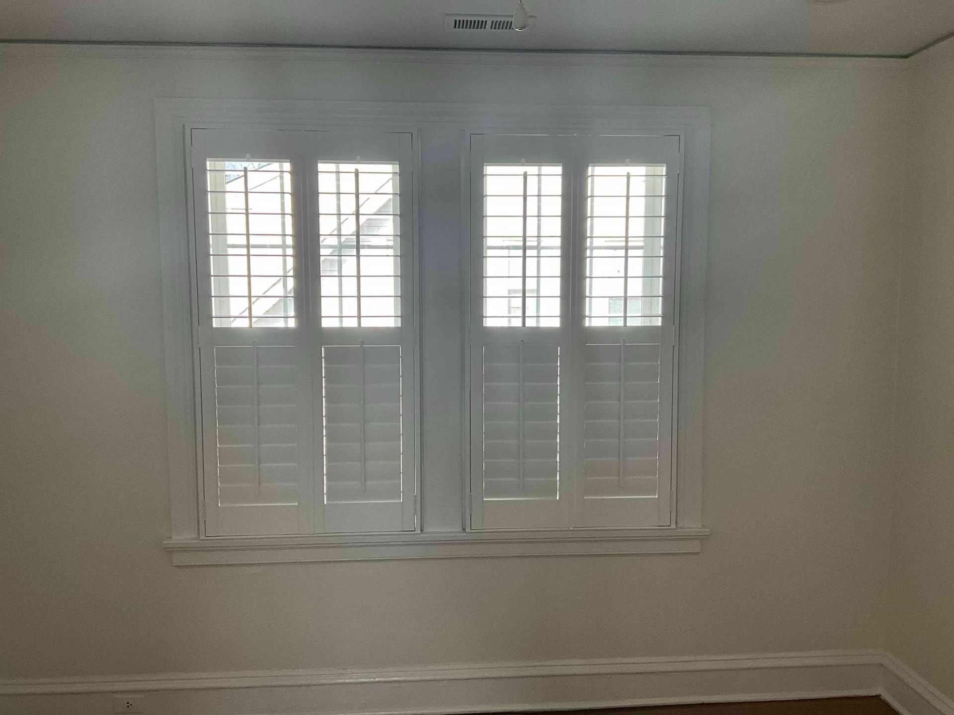 Empty room with white walls and shuttered window letting in soft daylight