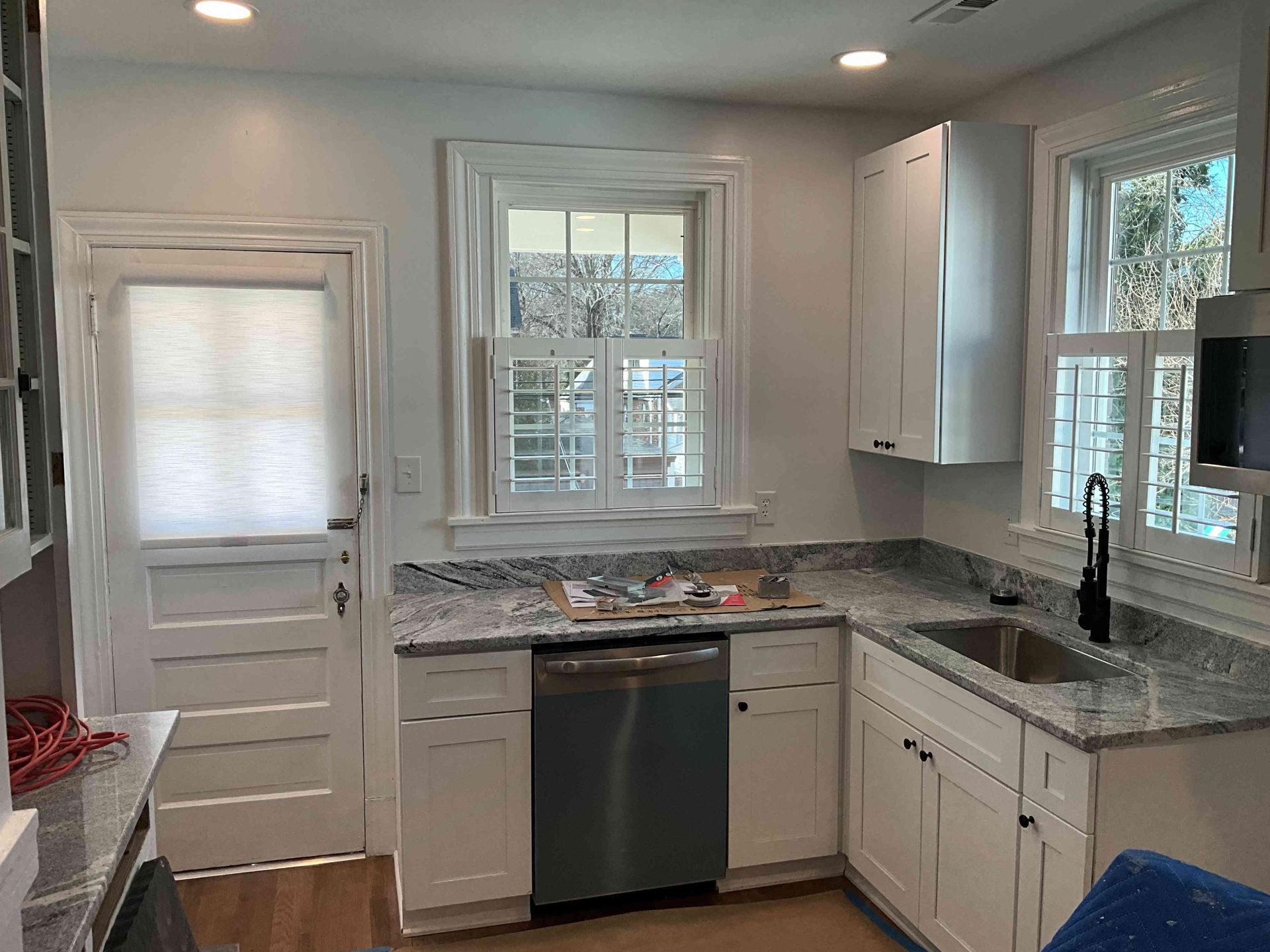 Bright white kitchen with granite counters, stainless dishwasher, sink, and windows letting in daylight
