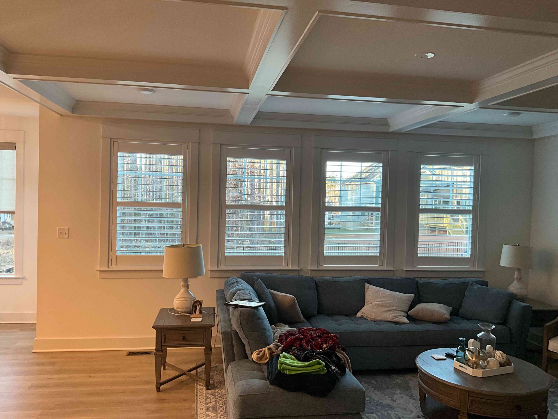 Living room with gray sectional sofa, coffee table, lamp, and large windows with blinds