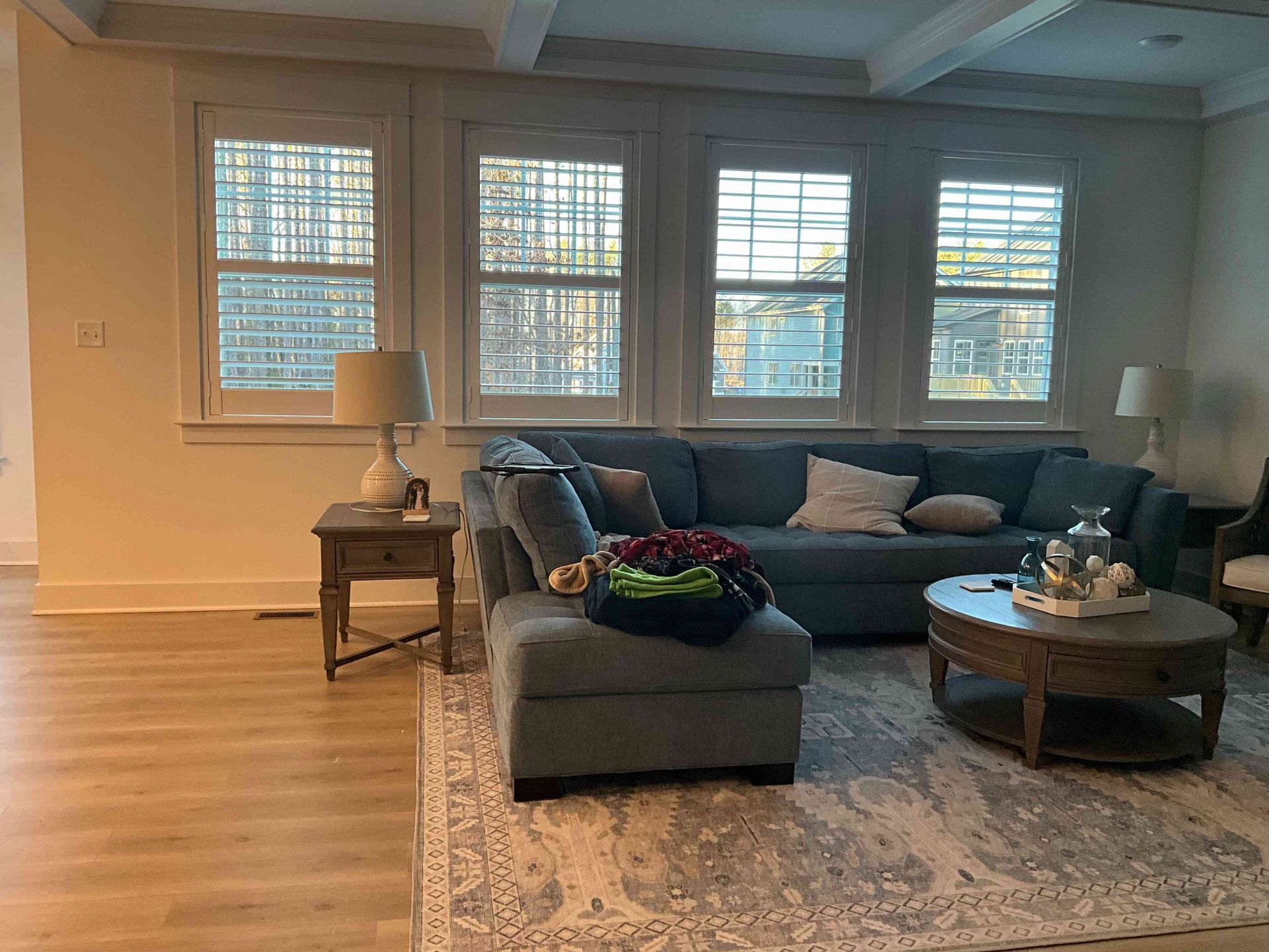Living room with gray sectional sofa, coffee table, lamp, and windows across the back wall