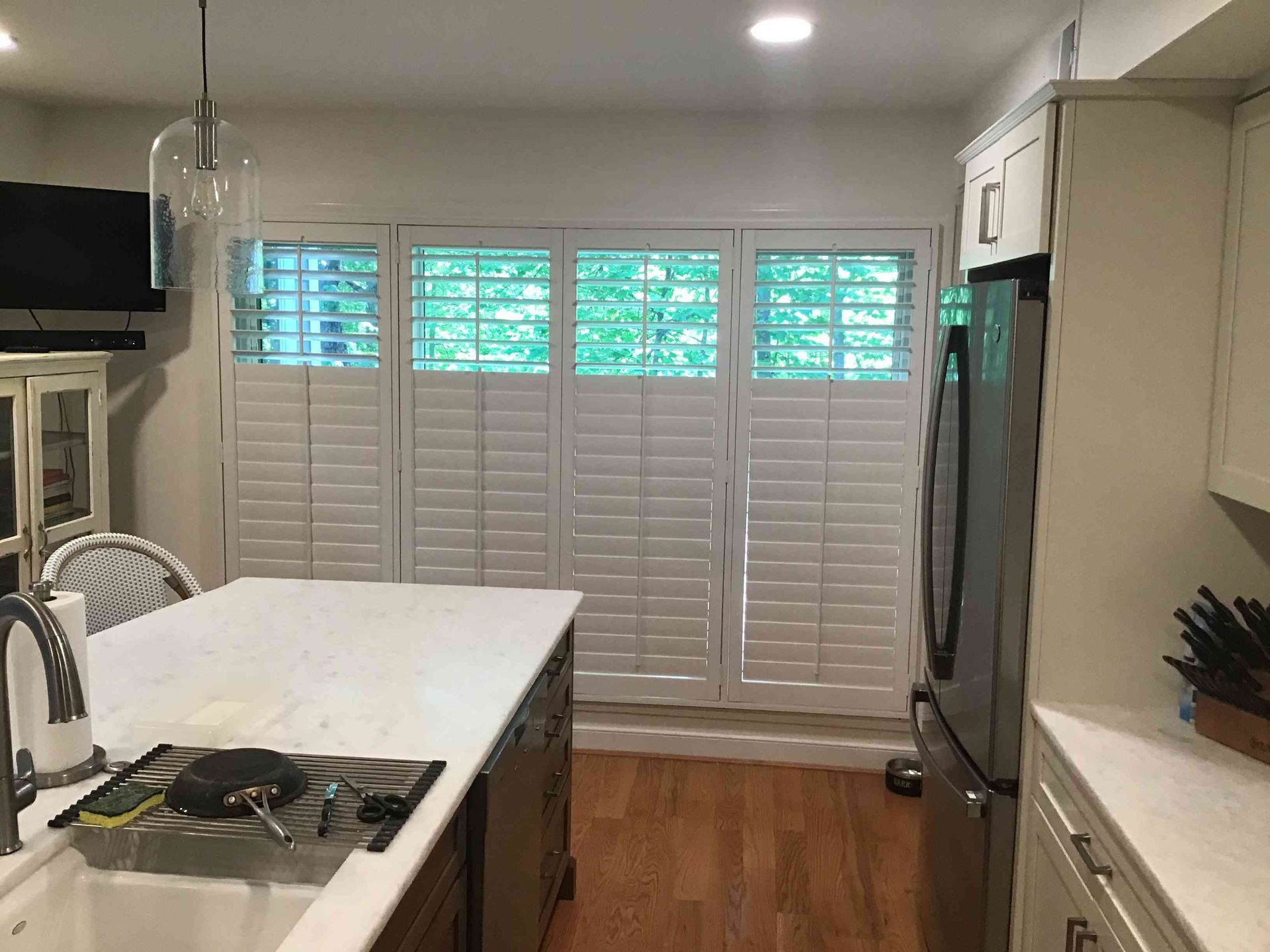 Modern kitchen with island, white cabinets, stainless fridge, and shuttered windows with blue light.